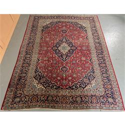 Persian Kashan red ground carpet, the field with scrolling floral design having a blue med...