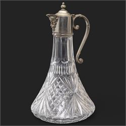 Composite plaque, depicting Sprites in a garden, with inset 'Arts and Commerce Promoted' medallion to reverse, 20cm x 33cm; together with a moulded glass Claret jug with silver plated mount H30cm 