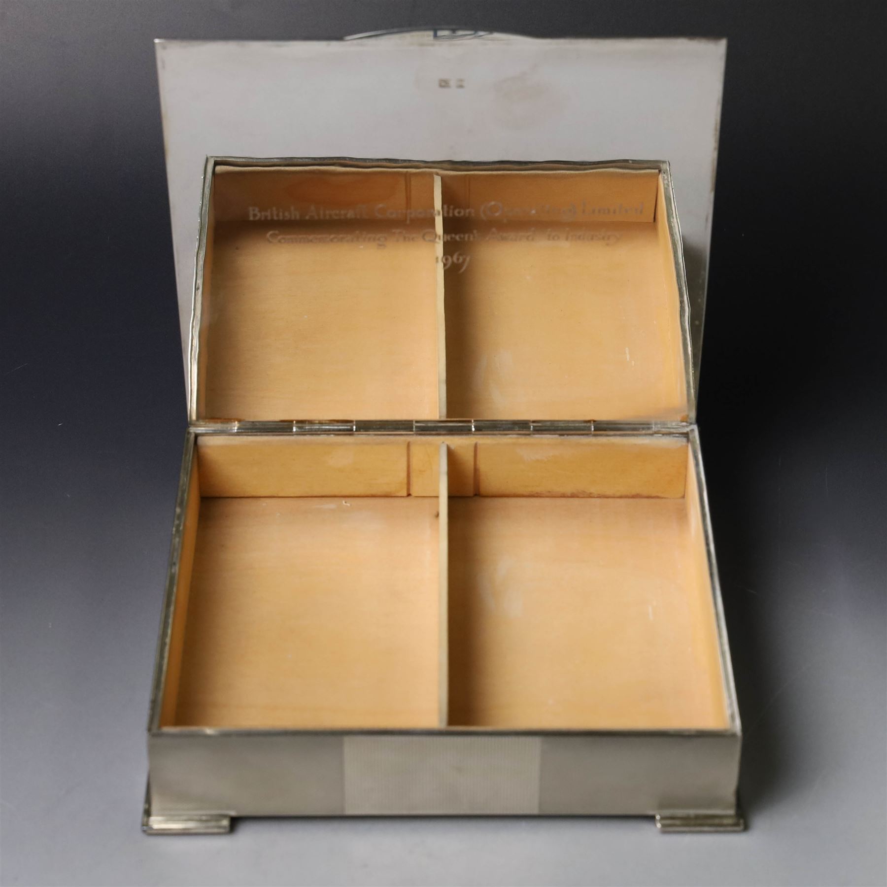 1960s silver mounted cigarette box, of rectangular form with engine turned decoration, upon four bracket feet, with presentation engraving to interior lid reading  'British Aircraft Corporation (Operating) Limited Commemorating the Queen's Award to Industry 1967, hallmarked James Geraghty, Birmingham 1965, with retailers mark for Asprey, W16.5cm, H4.5cm
