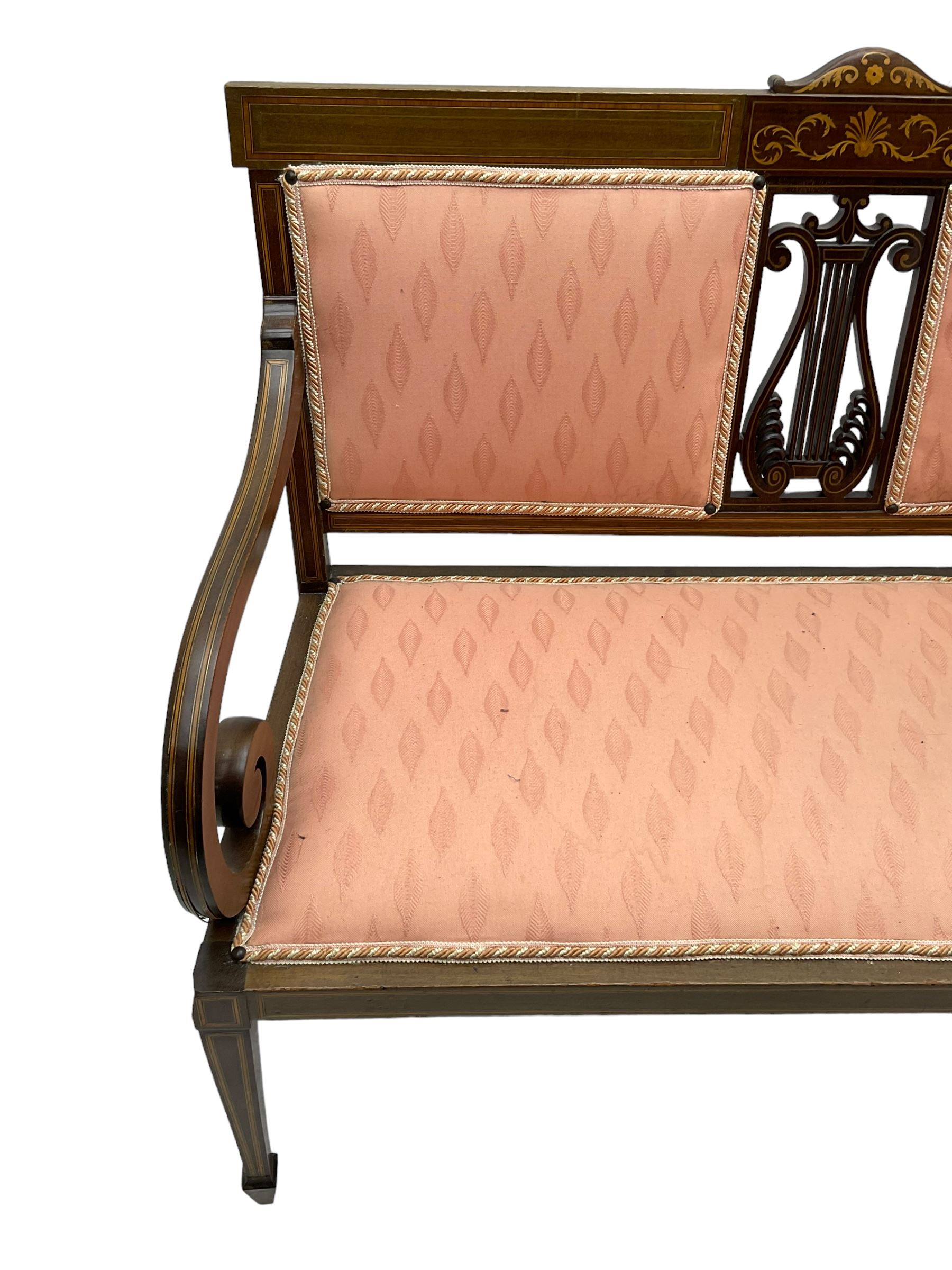 Edwardian inlaid mahogany two-seat settee or hall bench, the cresting rail inlaid with satinwood banding and boxwood stringing, central panel inlaid with scrolled leafy branches over pierced and carved lyre back, upholstered in peach fabric with repeating pattern, scrolled down sweeping arms, on square tapering supports with spade feet 