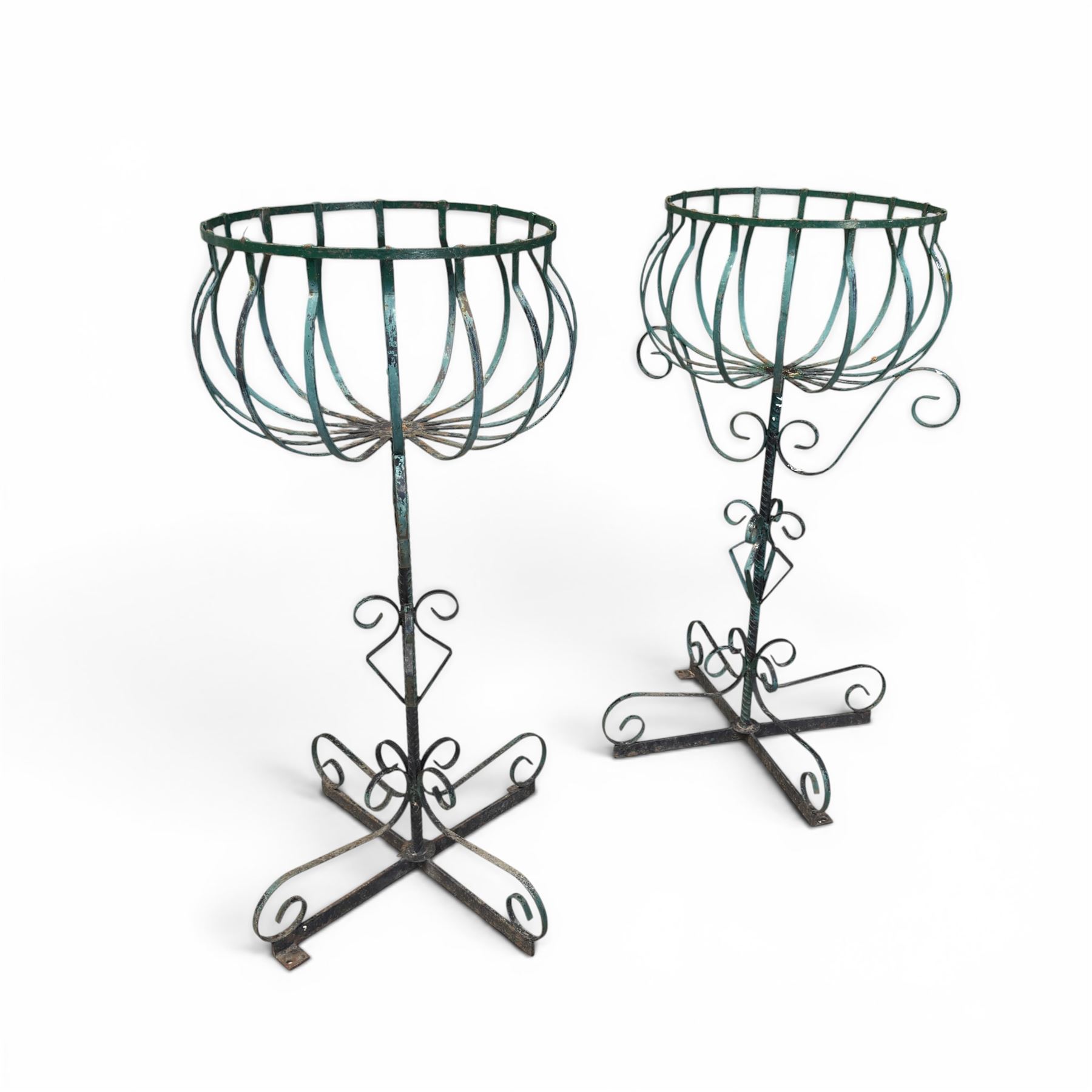 Matched pair of antique metal plant stands, each with circular strapwork basket tops, the scrollwork supports raised on an X-form base, in green painted finish with rustic patina