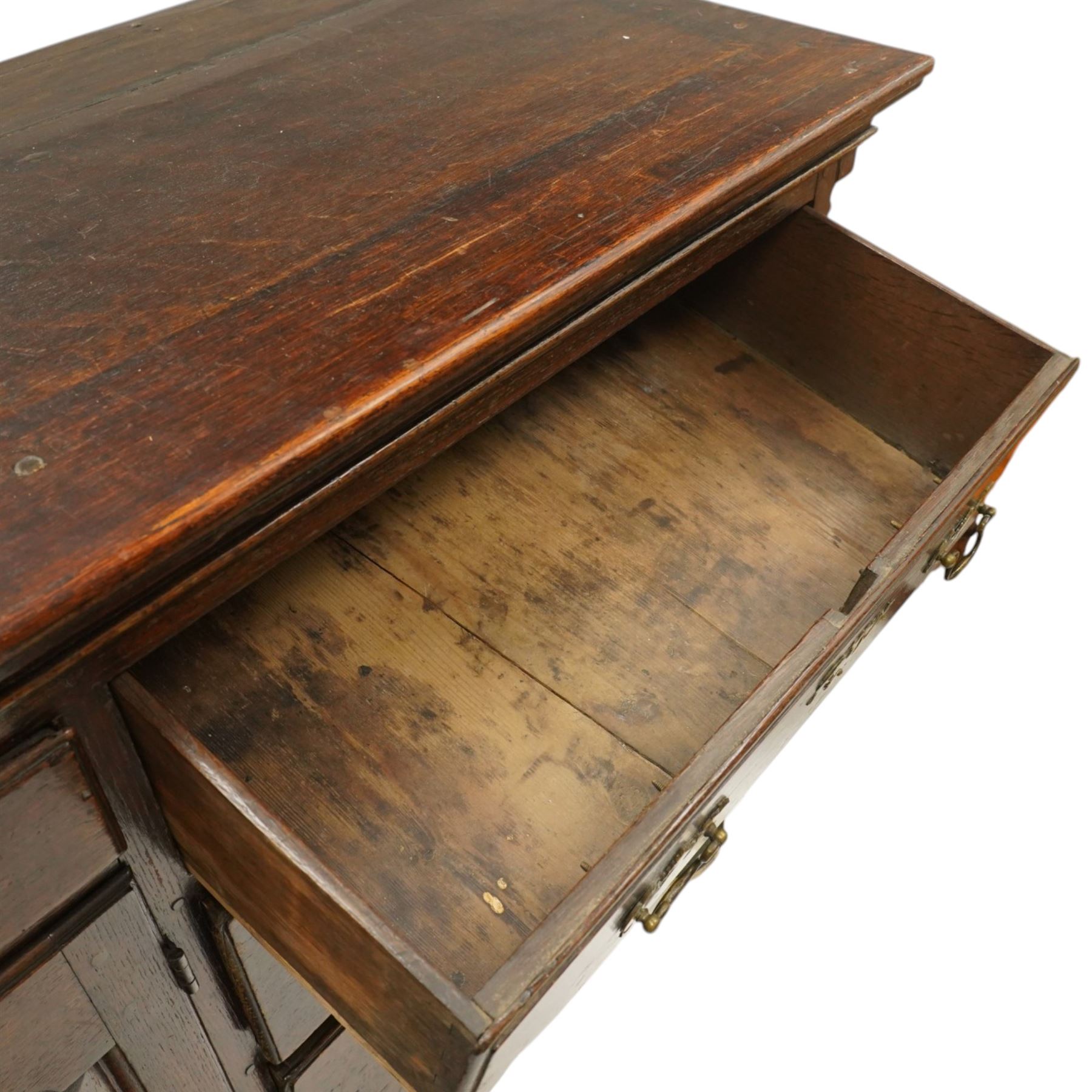 19th century Georgian oak long dresser base, rectangular plank top above a central frieze drawer over a fielded panel cupboard, flanked by three banks with quarter cantered pilasters, brass swan neck handles and escutcheons, raised on shaped bracket feet
