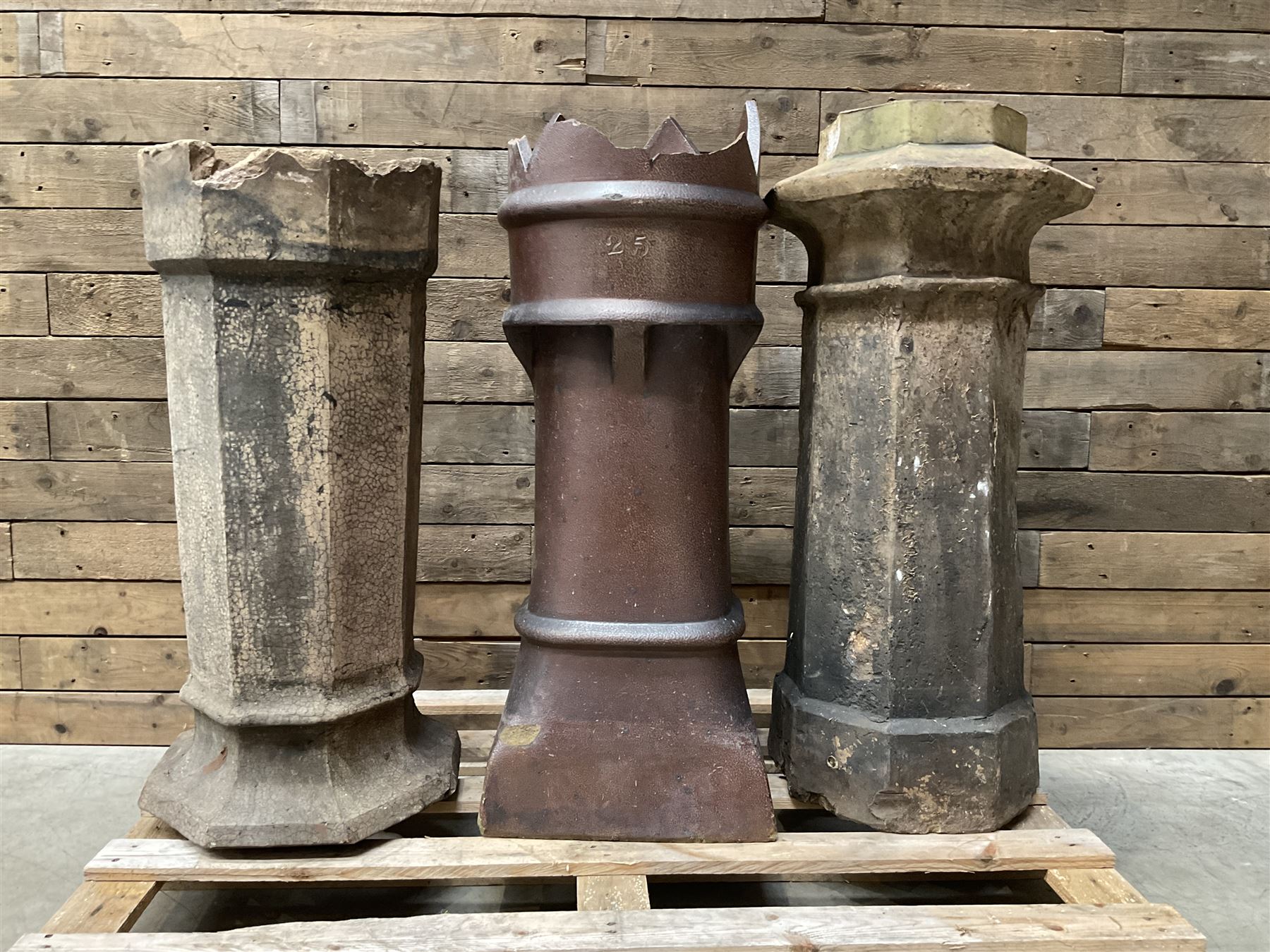 Collection of three Victorian and early 20th century reclaimed terracotta chimney pots, comprising: one cylindrical form with weathered, cracked glaze and flared octagonal base; one deep red cylindrical pot with fluted midsection and castellated rim, bearing moulded number ‘25’; and one tapering hexagonal example with wide flared rim and weathered patina. All with age-related wear and chips, consistent with use and outdoor exposure. Plus a selection of cast stone pieces including fountain 