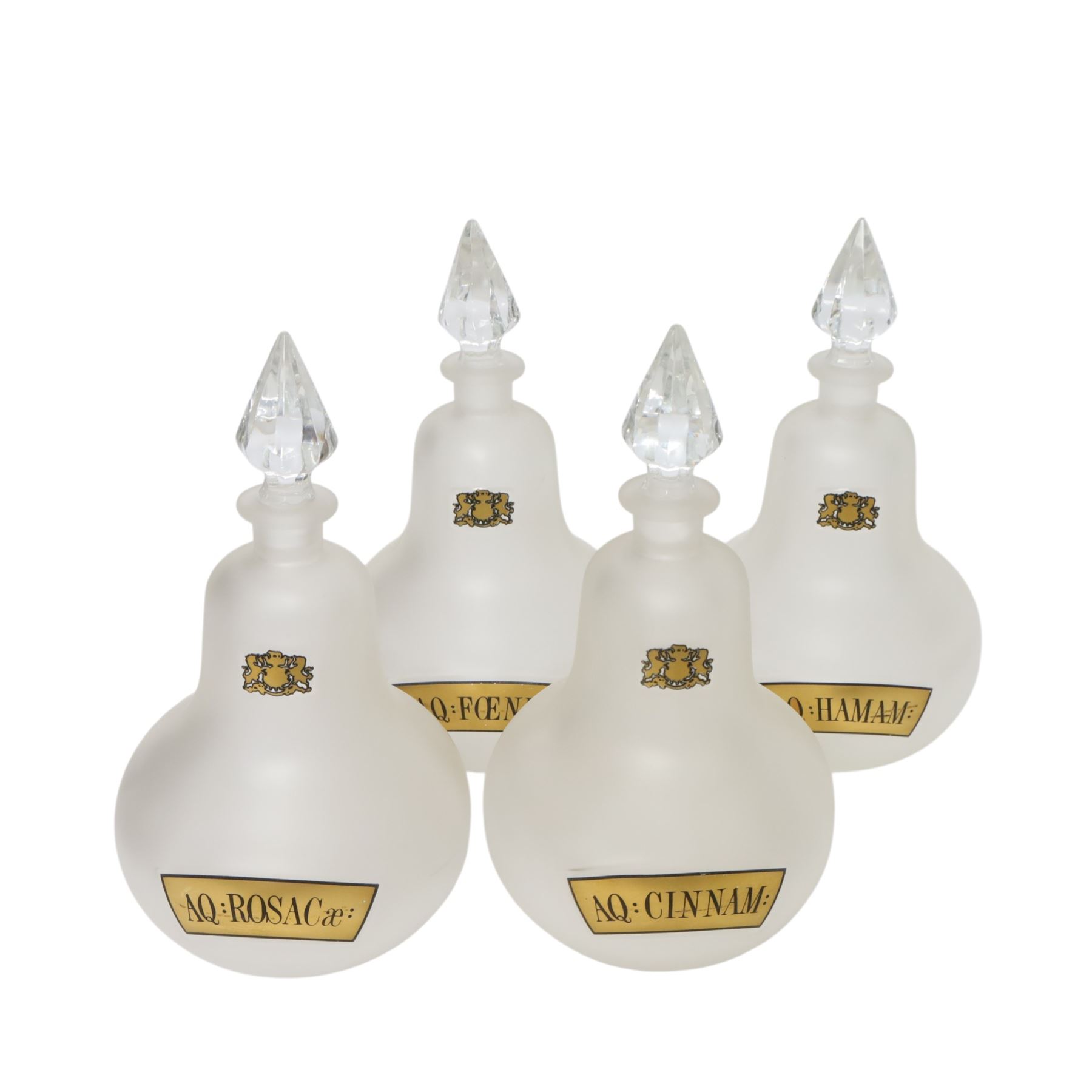 Set of four 20th century Royal Pharmaceutical Society white frosted glass bottles, of bellied form with clear cut glass spire stopper, each body bearing gilt label in Latin: AQ:CINNAM:, AQ:FOENIC:, AQ:HAMAM:, and AQ:ROSACae:, and gilt Royal Pharmaceutical Society crest to neck, H25cm

Provenance: From the collection of the family of Peter Green, a practising pharmacist whose career spanned the mid to late 20th century. During his professional life he managed pharmacies in Yeovil, Somerset, and later Selles Chemist in Filey, North Yorkshire, before purchasing and running his own business, Peter Green Pharmacy, located in the Market Place, Malton. The bottles were displayed as part of the traditional shop fittings in both the Filey and Malton pharmacies and were retained as part of his collection.