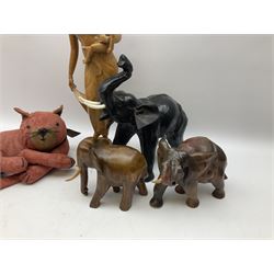 Carved wooden figure of a mother and child, H52cm, two carved wooden figures of elephants, and a further model of an elephant with leather ears, plus a doorstop modelled as a recumbent cat, in one box 