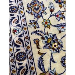 Central Persian Kashan hand-knotted carpet, ivory field with an all-over design of scrolling vines, lotus palmettes, and rosettes in shades of blue, gold, and brown within a blue ground border of palmettes and arabesques between multiple guard stripes