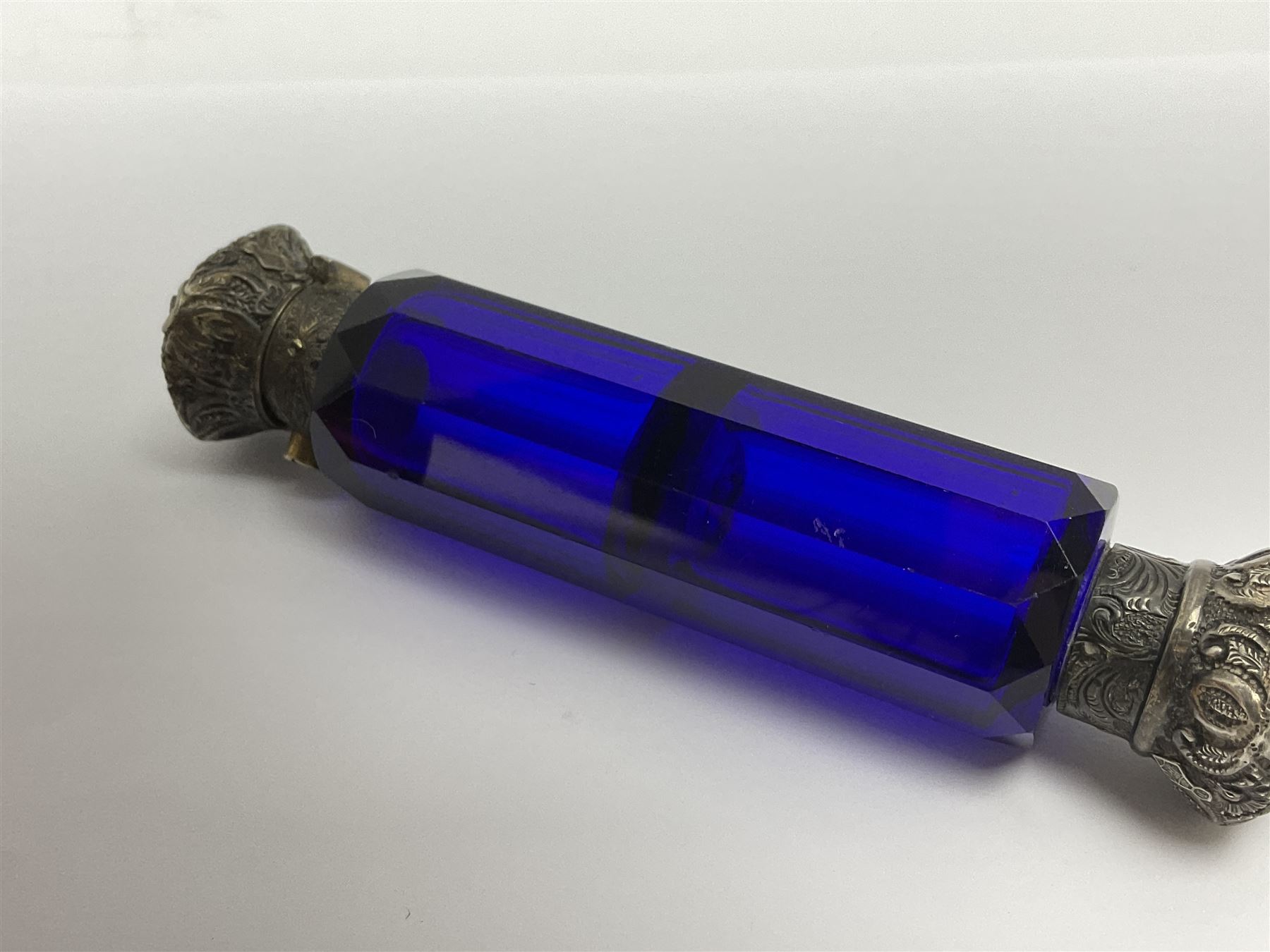 Late Victorian silver mounted ruby glass cylindrical scent bottle, with interior glass stopper, Birmingham 1900, makers mark worn, H8cm, together with a Victorian double ended cut blue glass perfume bottle mounted with white metal screw and flip caps decorated with foliate repousse detailing, H13.5cm