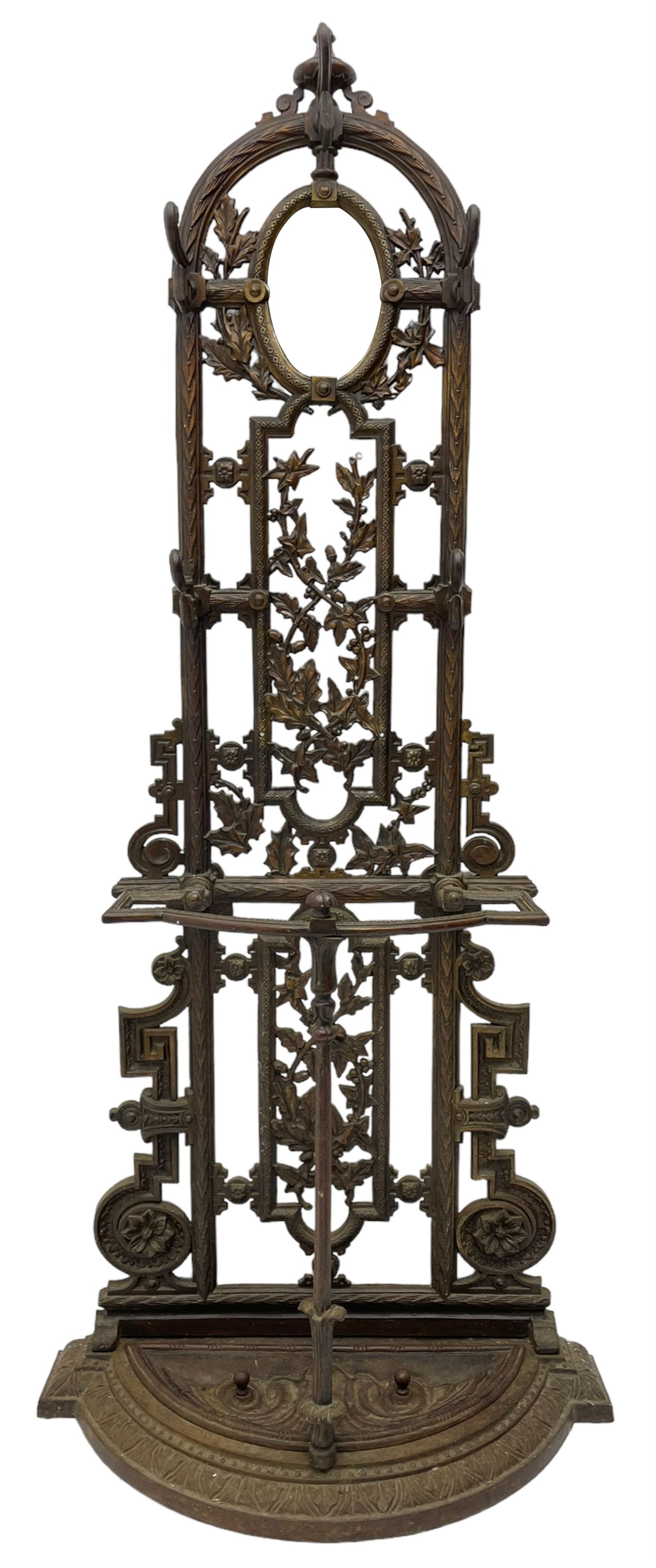 19th century cast iron hallway hat and coat stand, the arched frame decorated with overlapping foliage, central oval mirror surrounded by trailing oak leaves and acorns, with extending umbrella and stick stand, the curved plinth base decorated with acanthus leaves, with impressed and mounted R.d. lozenges