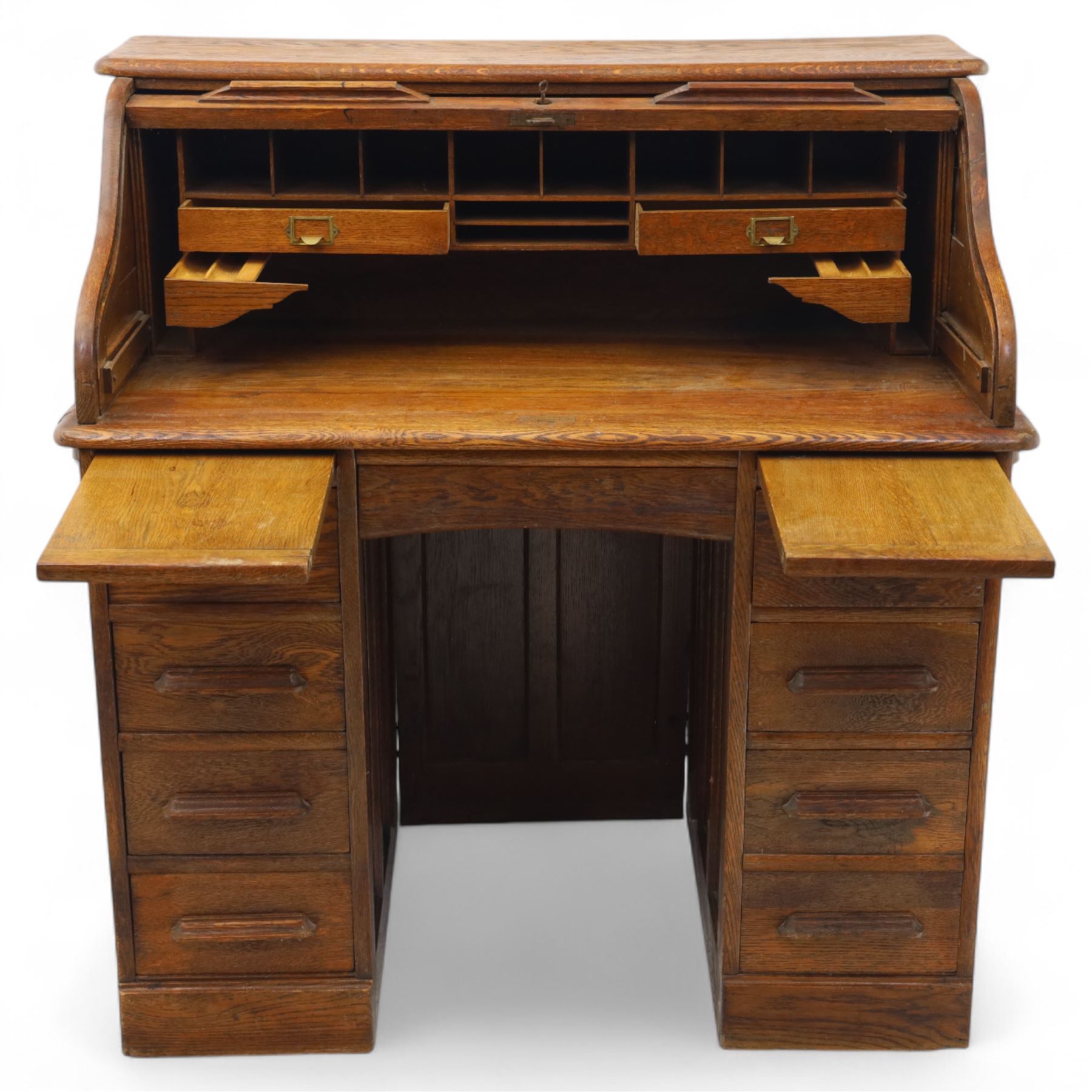 Early 20th-century oak roll-top desk with tambour shutter, enclosing a fitted interior of pigeon holes and small drawers, and pedestal base fitted with nine drawers with moulded handles, raised on plinth base 