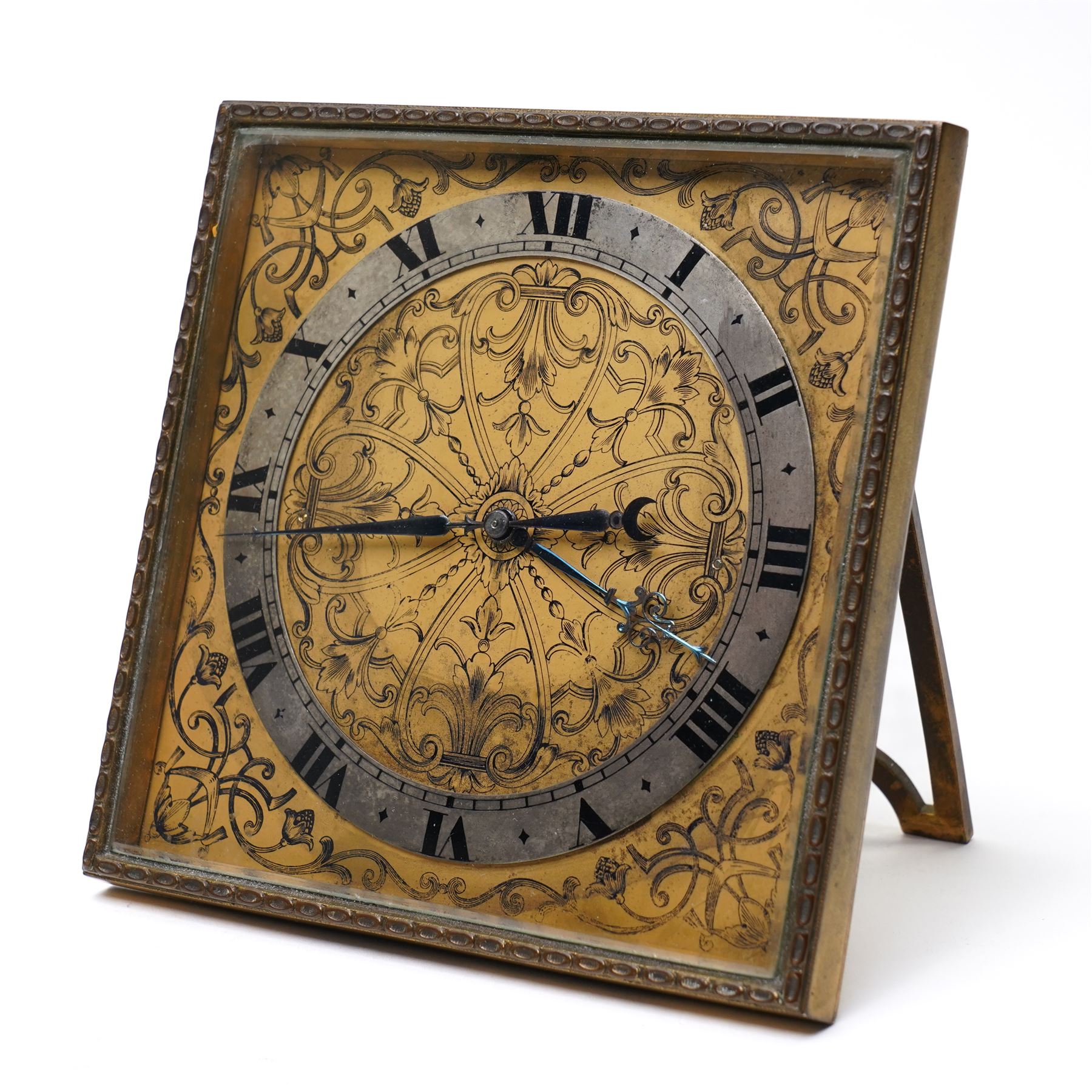 Early 20th century-Swiss bedside Strut Clock with an 8-day timepiece movement and balance escapement, four and a half inch square picture frame case with fine detail surround, gilt dial with exquisitely etched engraving to the corners and centre, silvered chapter with Roman numerals, inner minute track and elegantly fettled blue steel hands, wound and set from the rear.