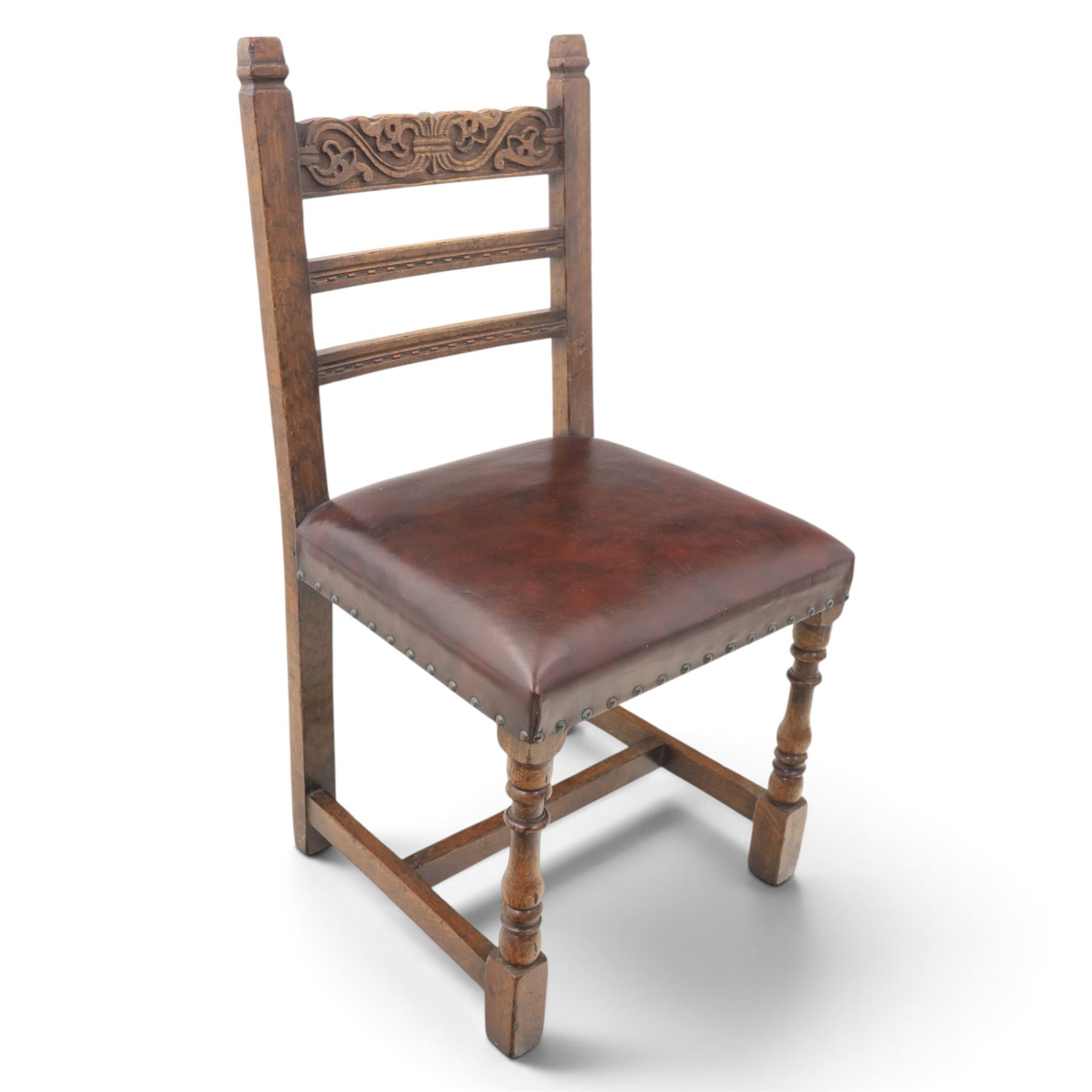 Craftsman made set of four solid oak dining chairs with leather seats, with carved cresting rail, on red leather seats with studded trim, raised on block and turn supports united by H-stretcher