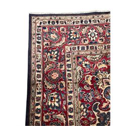 Persian Kashan indigo ground carpet, large central rosette medallion decorated with alternating palmettes, the surrounding field and spandrels with overall floral design depicting trailing branches and stylised plant motifs, crimson ground border with trailing floral pattern, enclosed within guard stripes 