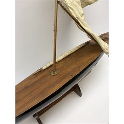 Pond yacht with part black painted mahogany hull and keel, working rudder and mast with three sails W90cm H95cm, loose mounted on mahogany stand