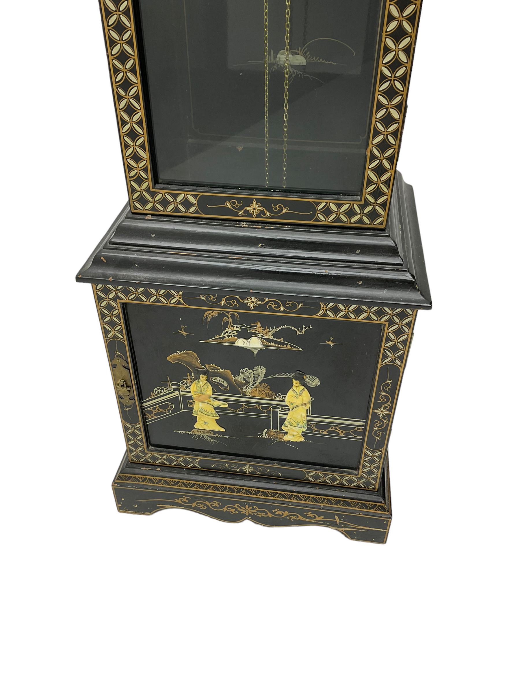 20th century 8-day chain driven black lacquered longcase clock - with a swans neck pediment and break-arch hood door, fully glazed trunk door displaying brass cased weights and pendulum, case sides, hood and plinth profusely decorated in gold relief and chinoiserie figures, brass break arch dial with an etched centre and silvered chapter ring, German two train movement striking the hours and half hours on two gong rods. With weights and pendulum.
