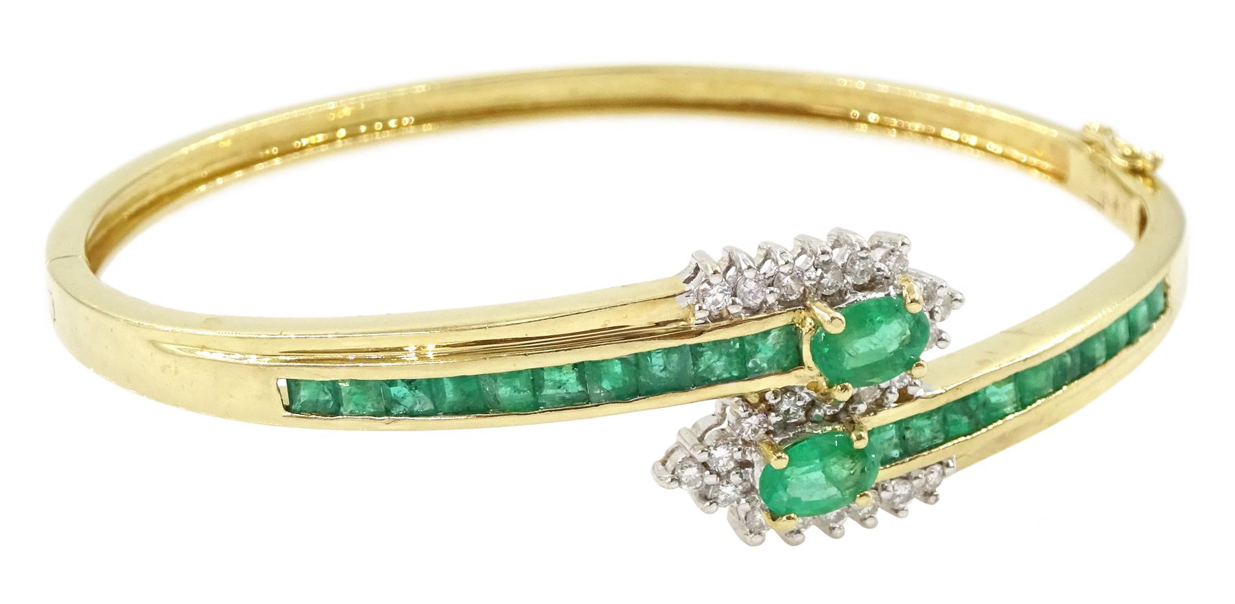 14ct gold emerald and diamond crossover bangle, two oval cut emeralds with round brilliant cut diamond surround, with channel set calibre cut emerald shoulders, stamped 585