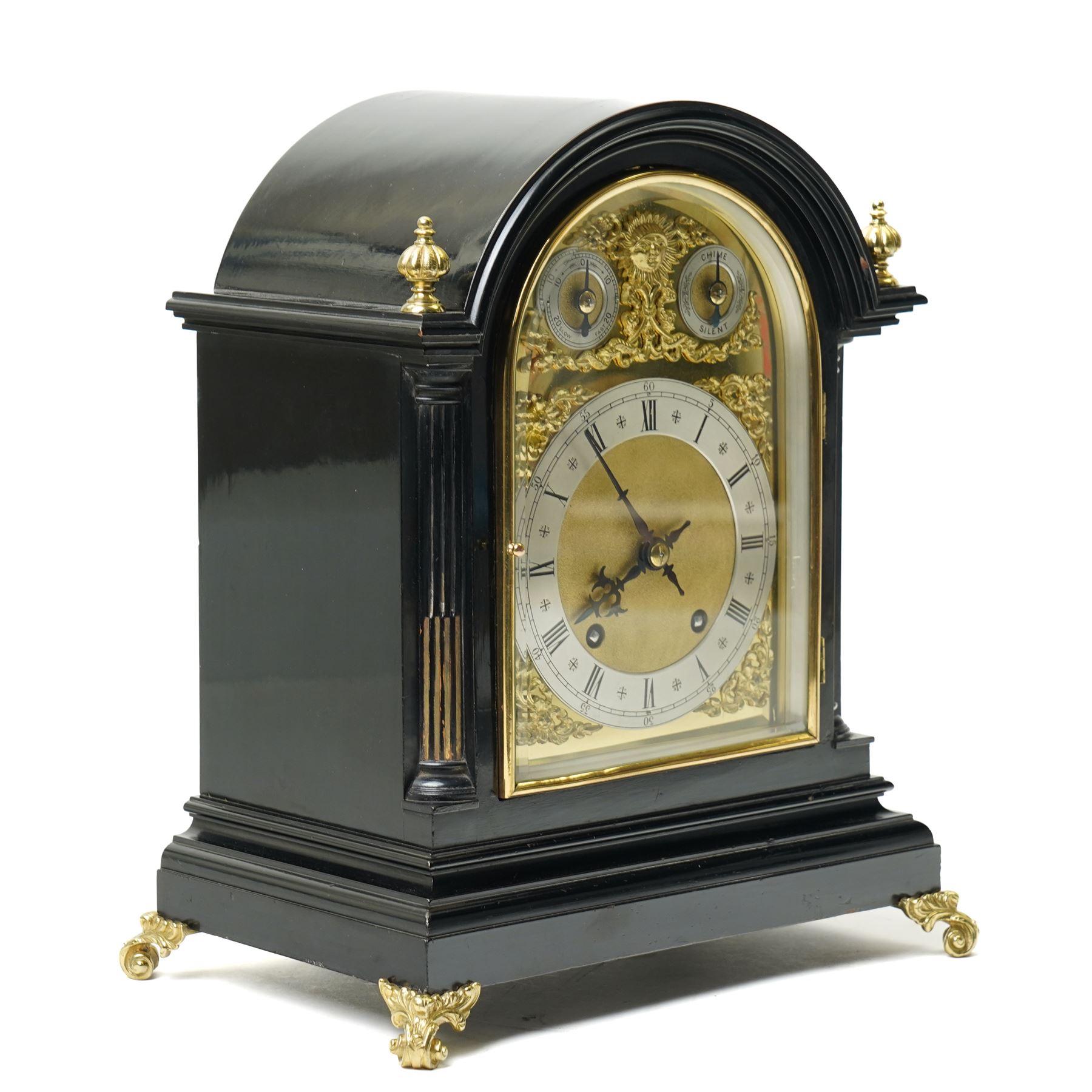 Winterhalder & Hoffmeier-8-day early 20th century mantel clock with an ebonised finish, break arch pediment and two matching brass finials, conforming glazed door with a cast brass bezel flanked by reeded quarter pilasters, on a moulded plinth with scroll feet, brass dial with cast spandrels and strike/silent and pendulum regulation dials to the arch, matted dial centre with a silvered chapter, Roman numerals  and gothic steel hands, dial pinned to a quarter striking movement sounding the quarters on two gongs and hours on one. With Pendulum.
