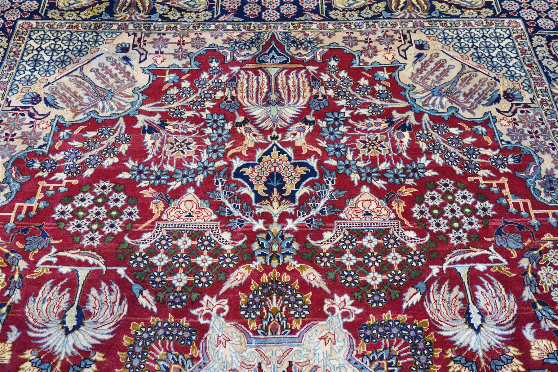 Central Persian Najafabad hand-knotted carpet, crimson field with a central elaborate cusped medallion with radiating floral motifs, surrounded by finely drawn scrolling vines incorporating stylized palmettes and rosettes, flowering plants and vase motifs, ivory spandrels similarly decorated enclosed by a dark indigo main border of floral arabesques between multiple guard stripes, with cotton fringe ends 