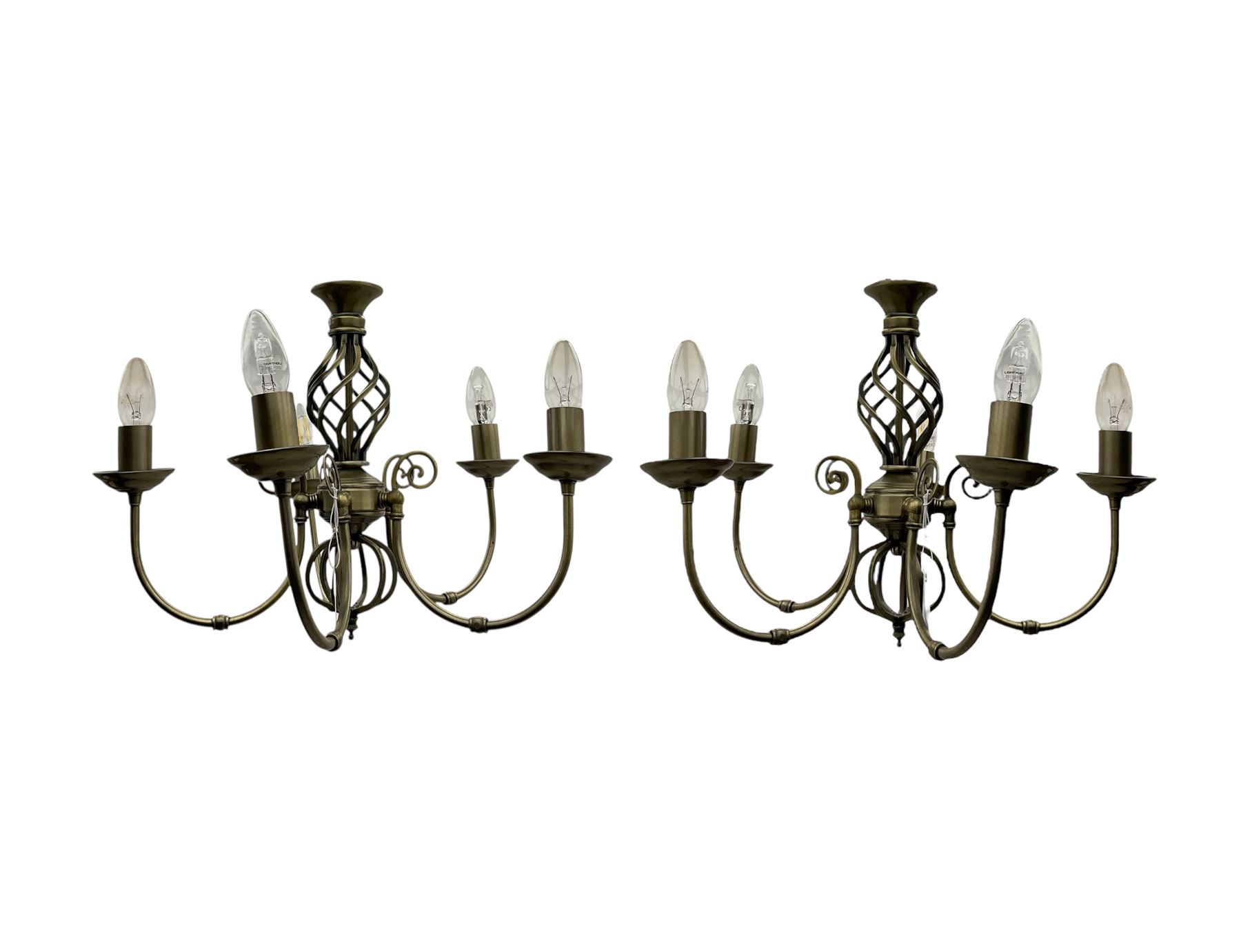 Pair of brass five-branch chandeliers, each featuring scrolling arms with candle-style light fittings, centred by a twisted openwork column, complete with ceiling roses and hanging chains