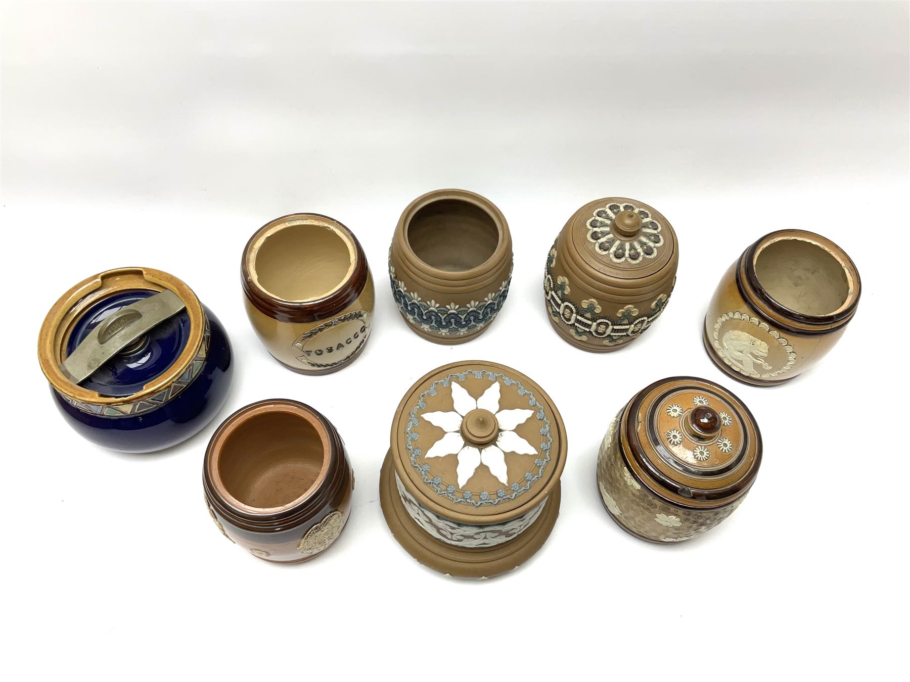 A group of Doulton Lambeth and Royal Doulton tobacco jars, most with relief moulded foliate decoration, (four examples lacking covers), largest example H15cm. 