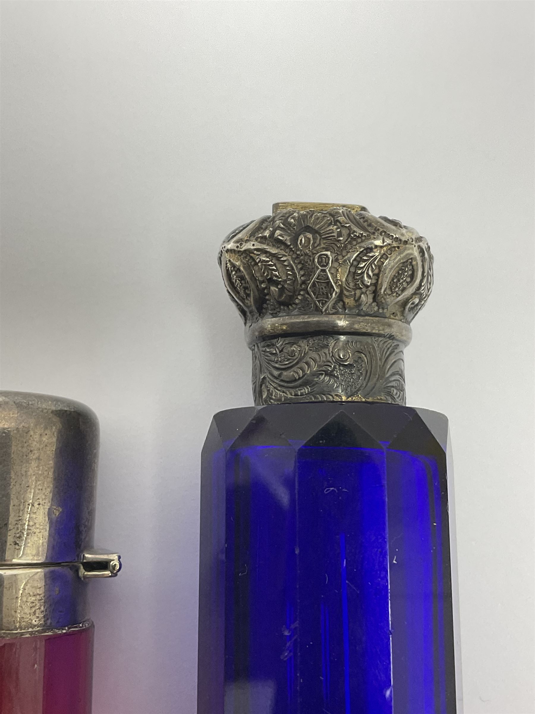 Late Victorian silver mounted ruby glass cylindrical scent bottle, with interior glass stopper, Birmingham 1900, makers mark worn, H8cm, together with a Victorian double ended cut blue glass perfume bottle mounted with white metal screw and flip caps decorated with foliate repousse detailing, H13.5cm