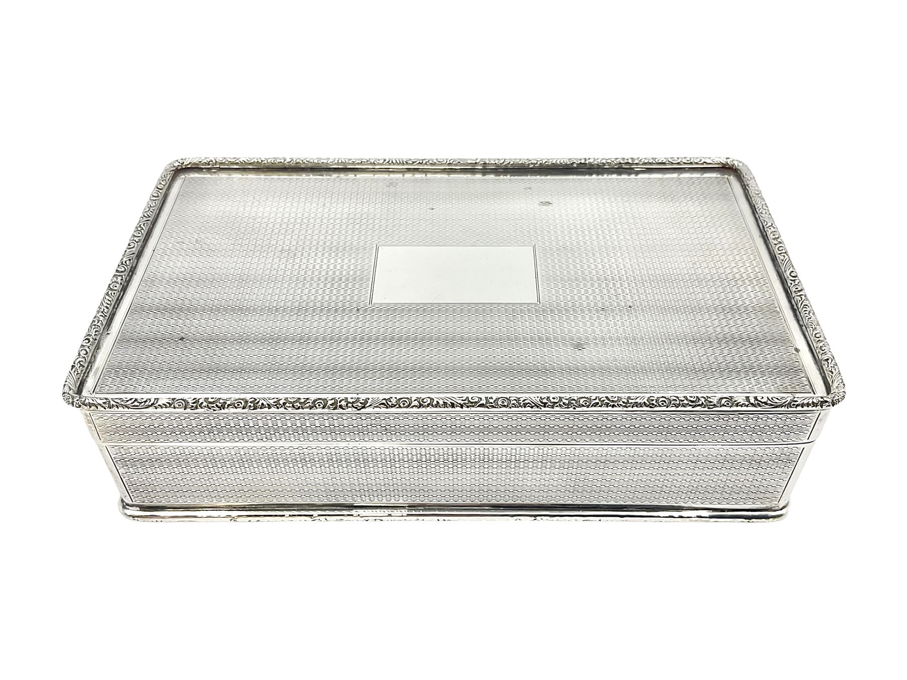 1920's silver table cigarette box, of rectangular form with engine turned decoration to the exterior, the hinged cover with central vacant rectangular panel and raised foliate rim, opening to reveal a gilt interior with later plush lining, hallmarked Charles Henry Dumenil, London 1923, H3.5cm L14.5cm D8.5cm