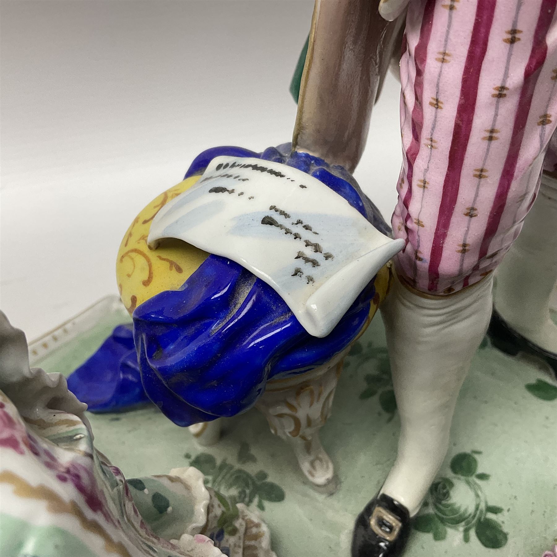 20th century Naples figure group, modelled as a seated female figure playing the lute seated, before a male figure stood holding a sheet of music, each in period dress, upon an oval base with gilt heightened scroll edge, with crowned N mark beneath, H31.5cm L33cm
