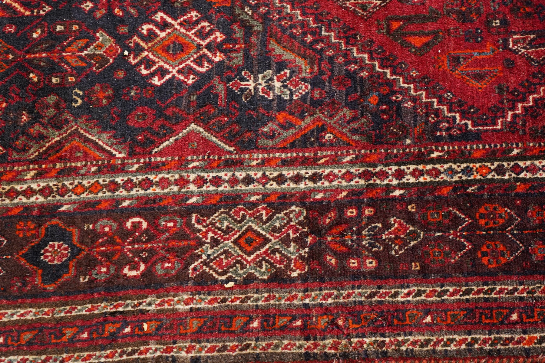 Large Persian Shiraz crimson ground carpet, the busy field decorated with a geometric pole medallion surrounded by stylised plant motifs with contrasting indigo spandrels and geometric-woven guard bands
