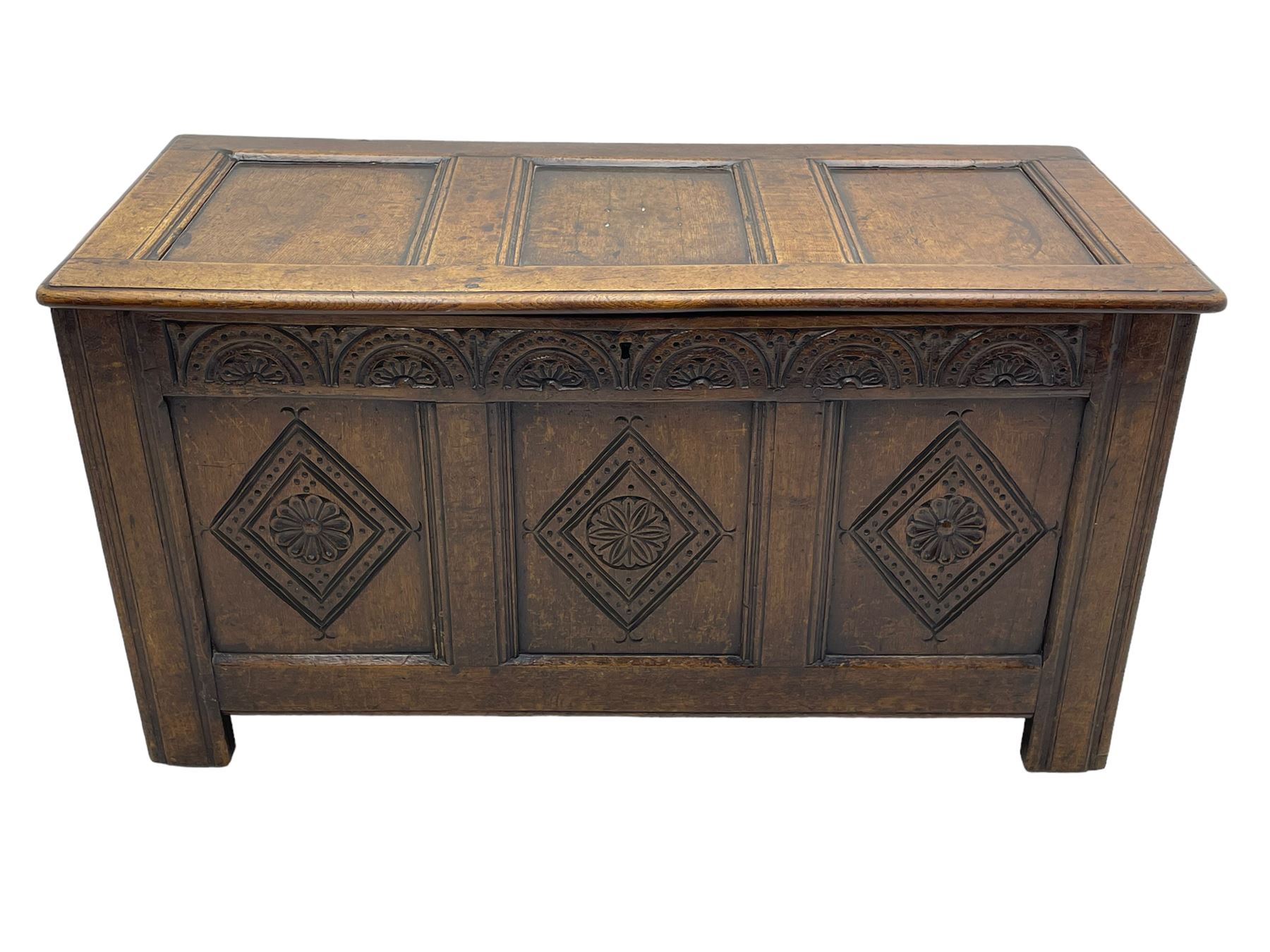 18th century oak coffer or chest, rectangular triple panelled hinged top with moulded edge enclosing main compartment and candle box, the frieze carved with repeating concentric lunettes and foliate patterns, the front fielded panels decorated with lozenges containing central flower heads, on stile supports