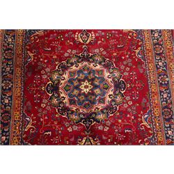 Persian Kashan hand-knotted rug, madder red ground centred by circular floral medallion with pendants, surrounded by scrolling vines, palmettes and flowerheads, dark navy spandrels, enclosed by dark navy floral border with multiple guard stripes