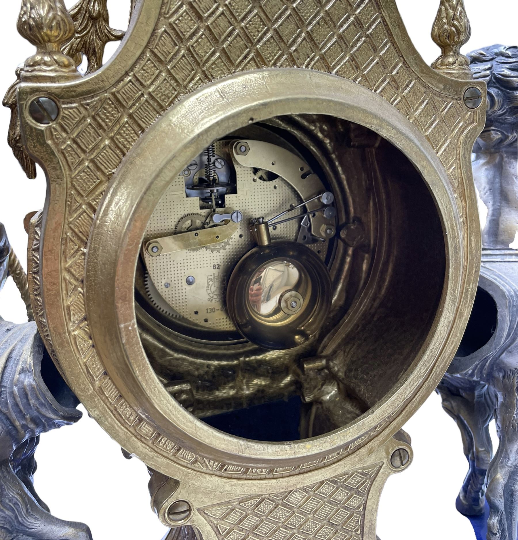 A 20th century continental gilt metal Lyre mantle clock with a pair of matching six light candelabra, spring driven movement housed in a gilt drum case on a brass and cobalt blue base with paw feet, two bronzed metal figures of mythological cherubs with animal legs and cloven hooves supporting a festooned garland swag, eight-day twin barrel striking movement with a floating lever balance escapement, striking the hours and half-hours on two bells, white enamel dial with roman numerals, minute track and pierced steel hands, dial inscribed “Imperial”. 