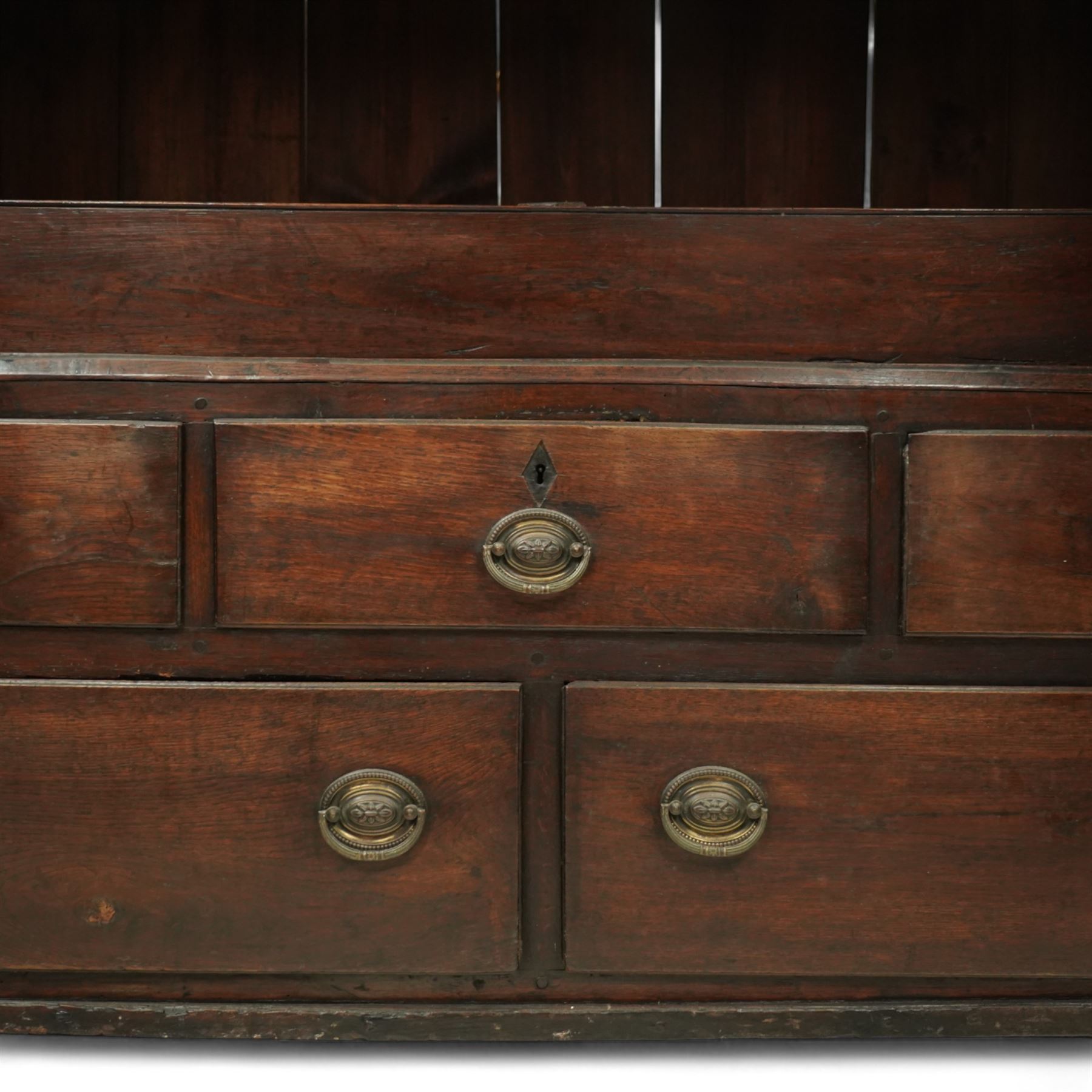 18th century oak dwarf press cupboard, the upper section with twin arched panel doors above three short and two long drawers, each with brass plate handles, shaped apron and stile feet, of compact country form