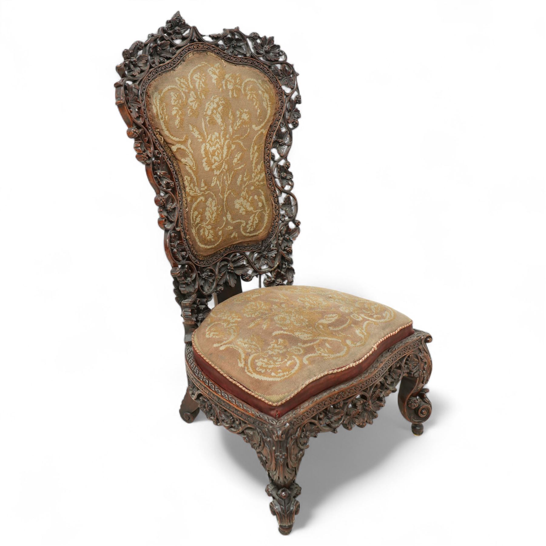 Late 19th century Anglo-Indian carved hardwood nursing chair, cartouche-shaped back, pierced fruit vine carved frame, gros-point tapestry upholstered seat, on carved scroll legs 