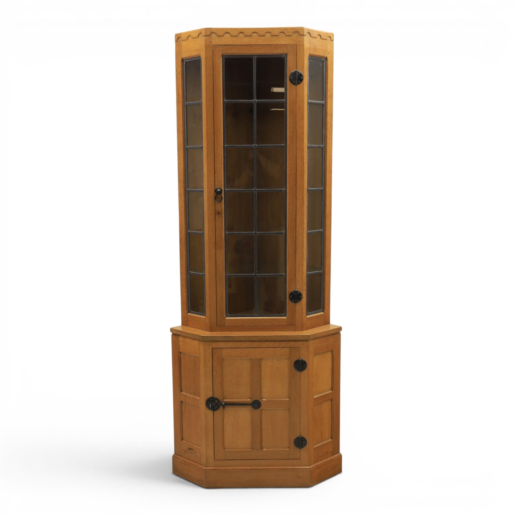 Mouseman - oak floor standing corner cabinet, scalloped cornice above a leaded glass cabinet, blackened metal hinges and latches, with carved mouse by the workshop of Robert Thompson of Kilburn