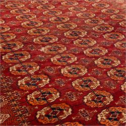 Vintage Bokhara hand-knotted rug, madder field woven in rows of octagonal Tekke guls arranged in vertical columns, each enclosing angular cruciform devices and tribal motifs, divided by narrow indigo lines, within multiple geometric borders incorporating stepped lozenges and latch hook devices, with cotton fringe ends 