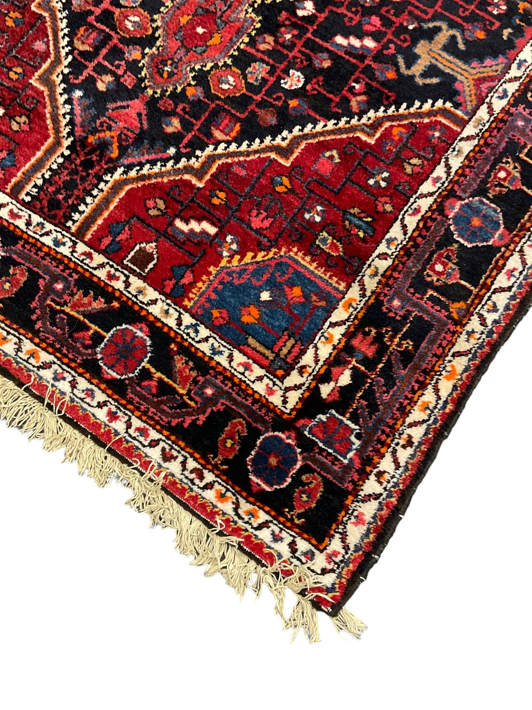 Persian Hamadan red and indigo ground rug, central lozenge medallion with extending poles, the field decorated with interlaced branches and flowerheads, guarded border with stylised floral motifs