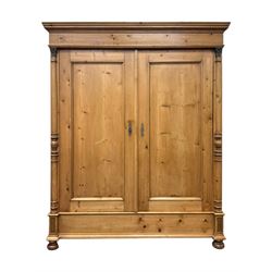 Large 19th-century Continental polished pine double wardrobe, panelled back and doors revealing brass hanging rod, flanked by half-turned columns with Corinthian capitals supported on bun feet