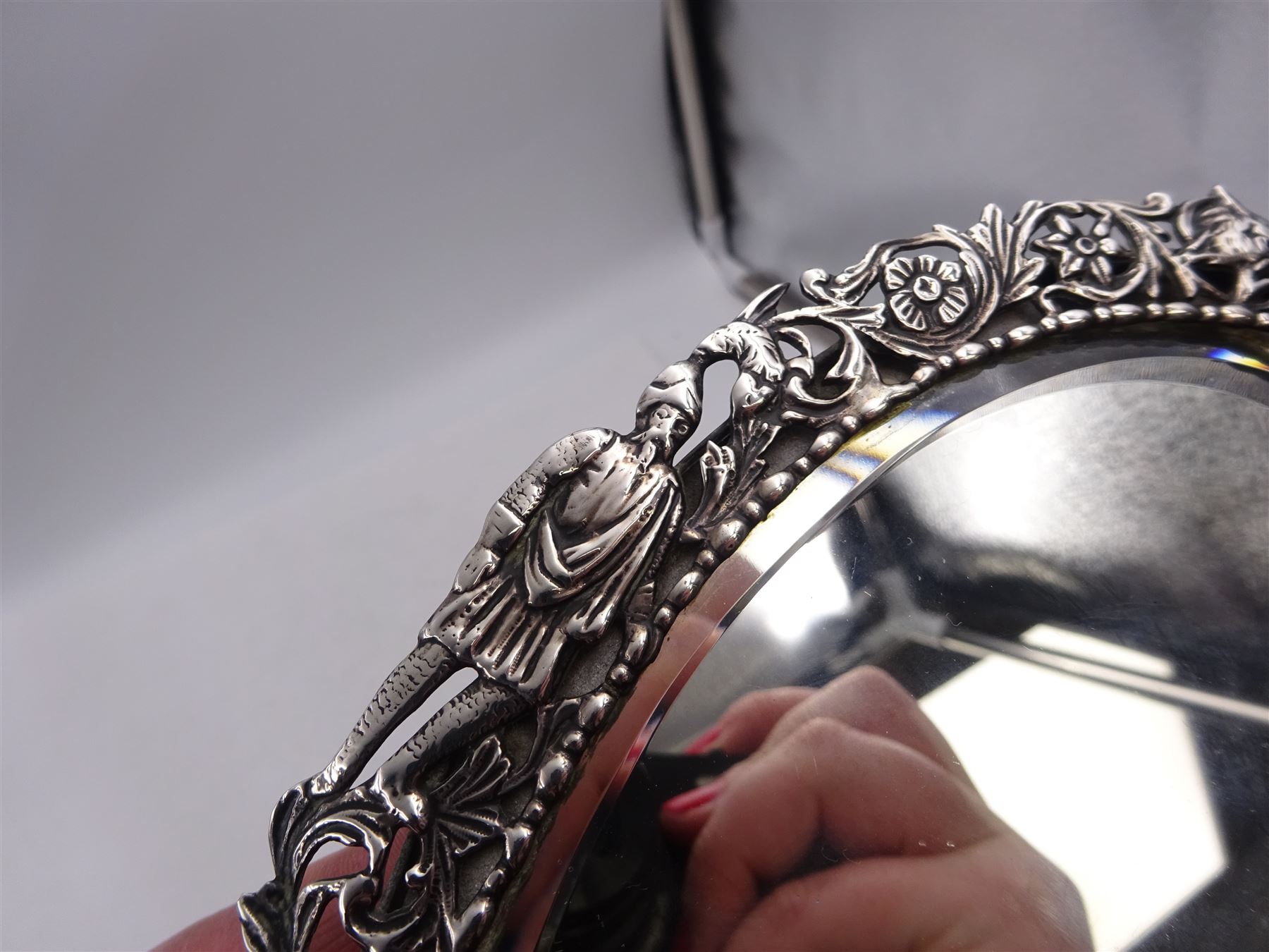Continental silver miniature dressing table/wall mirror, of oval form with bevelled mirror plate, surrounded by a bead and dart rim, with pierced scrolling floral border with a standing cavalier to either side and the bust of a cavalier to the base, H17.7cm
