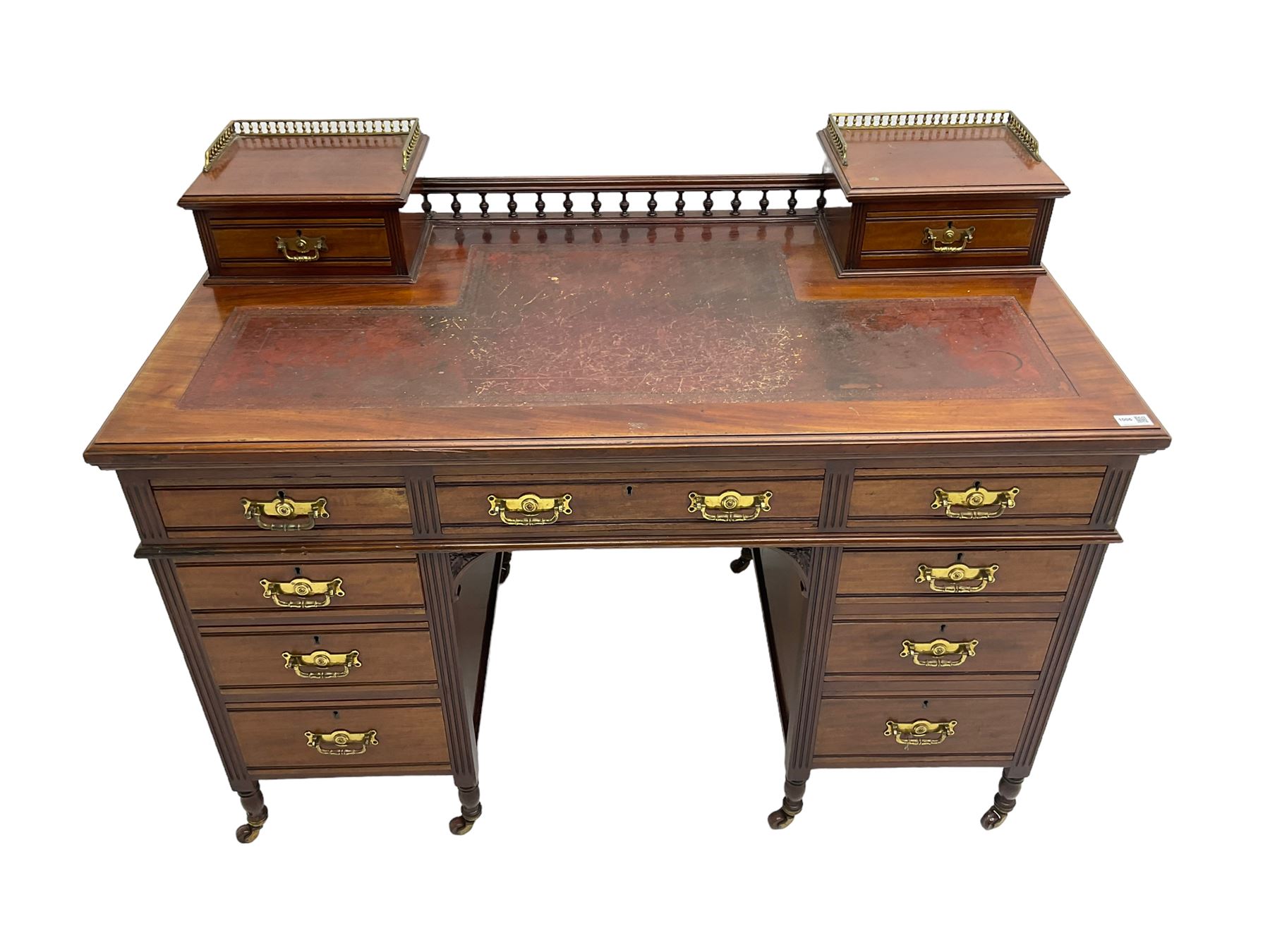Maple & Co - Edwardian mahogany twin pedestal desk, the raised back with spindle gallery and open shelf to centre flanked by two trinket drawers, rectangular top with inset writing surface, fitted with one long and eight short graduating drawers flanked by fluted uprights, raised on brass and ceramic castors, stamped to central drawer