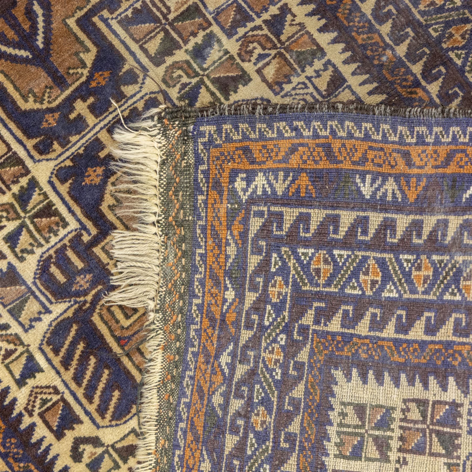 Baluchi design wool rug, with three geometric medallions on a cream field, enclosed by multiple dark blue, brown and rust geometric borders with fringed ends