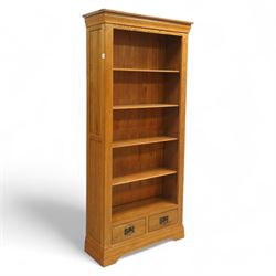 Contemporary oak bookcase, with moulded cornice above open shelved interior, fitted with four adjustable shelves and two short drawers with inset brass handles, panelled sides, plinth base