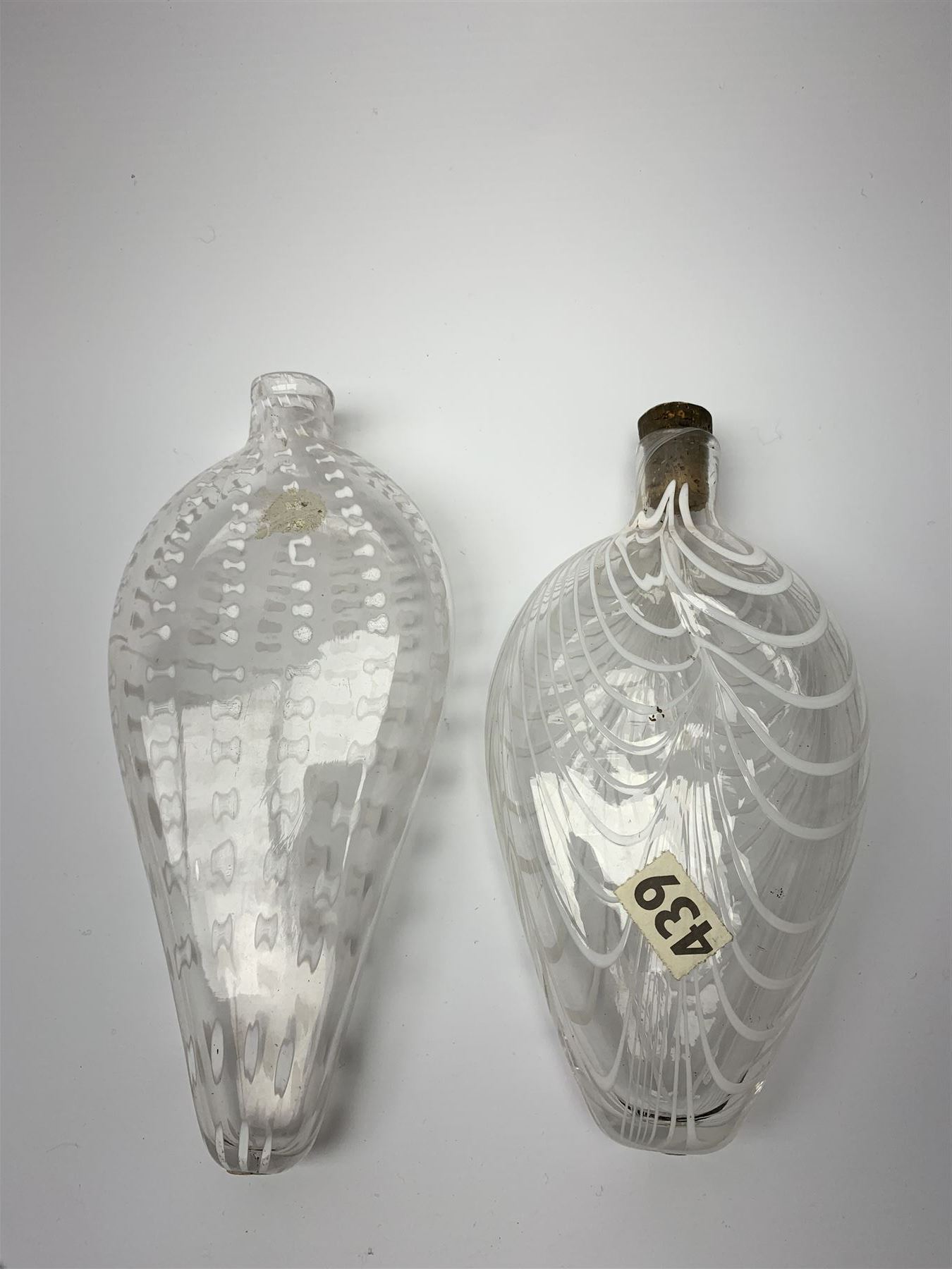 19th century Nailsea glass flask of compressed ovoid form, the clear body with opaque white combed decoration, H21cm, together with another similar example decorated with enamelled stylised bands, H23cm
