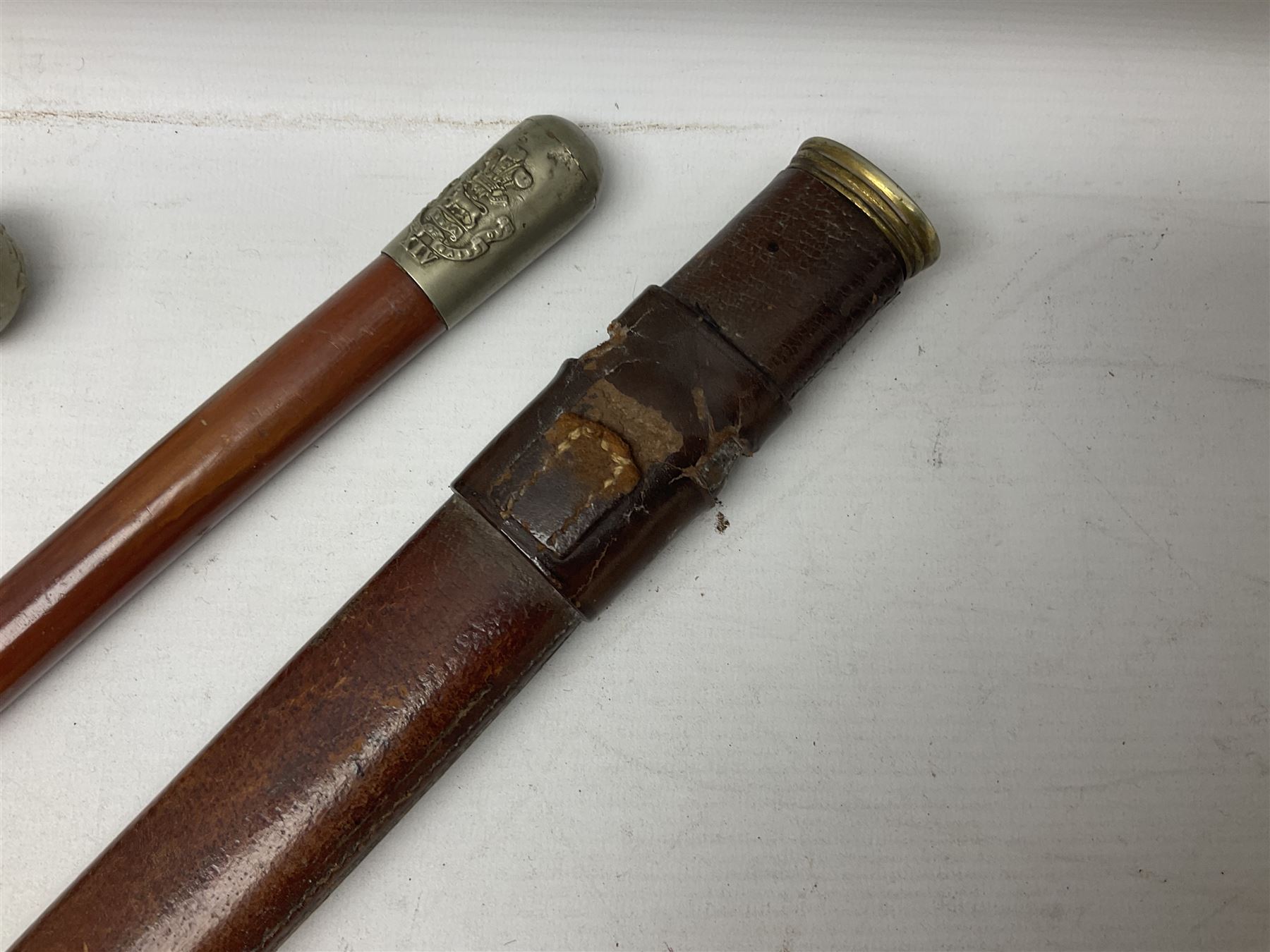 George V 1897 pattern Army Officer's sword by Henry Wilkinson Pall Mall London, the 82.5cm 'London Made' blade etched to both sides with Royal Crests and cyphers etc, pierced half-basket hilt with wire-bound fish skin grip and remains of leather knot strap; in leather covered field service scabbard L101cm overall; and two 14th Prince of Wales Own swagger sticks (3)