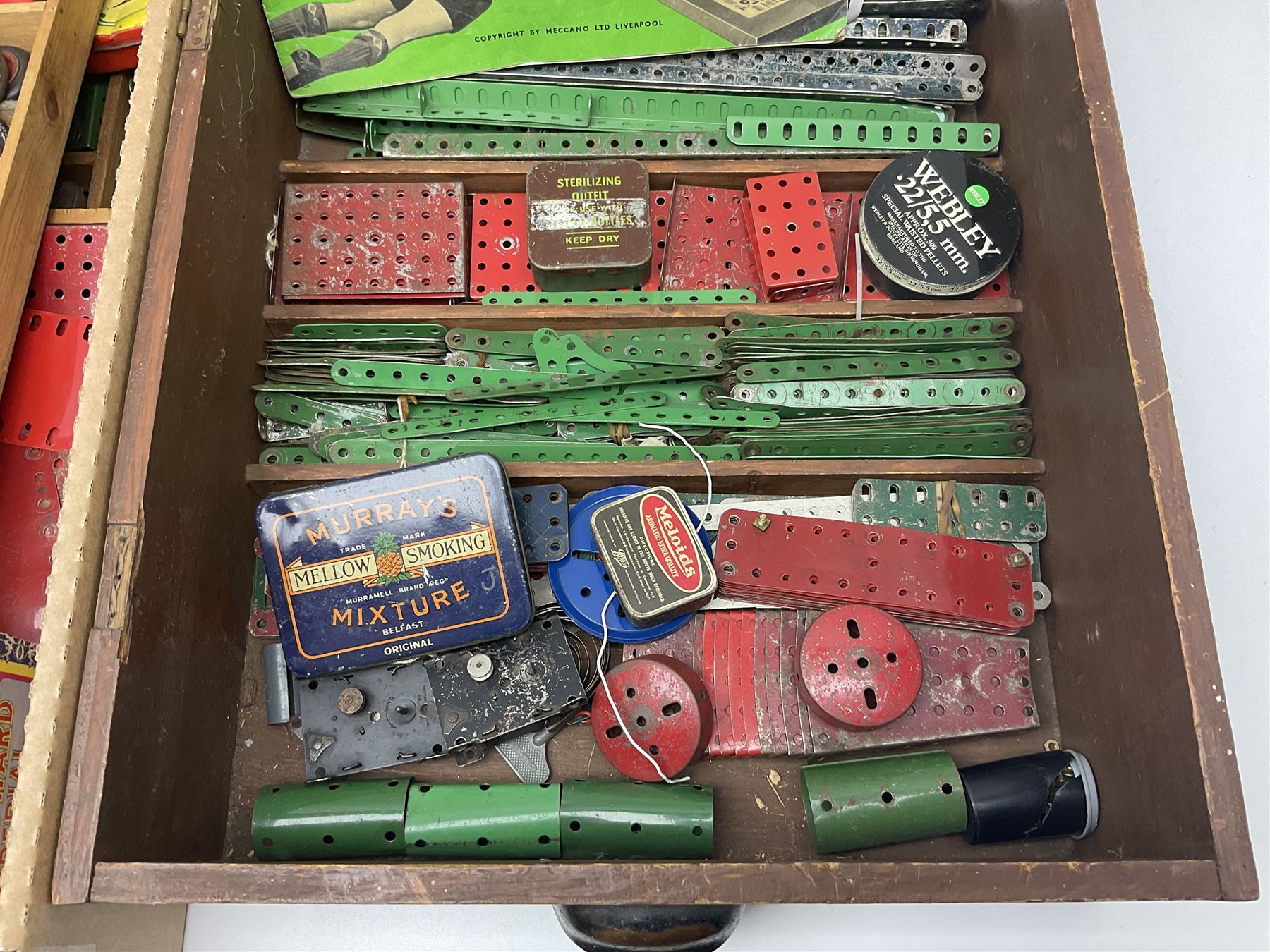 Meccano - large quantity of loose parts including various plates and strips, flanged plates, pulleys, axle rods and crank handles, wheels and tyres, gear wheels, brackets, nuts & bolts, various manuals; predominantly red and green; some in compartmentalised wooden trays