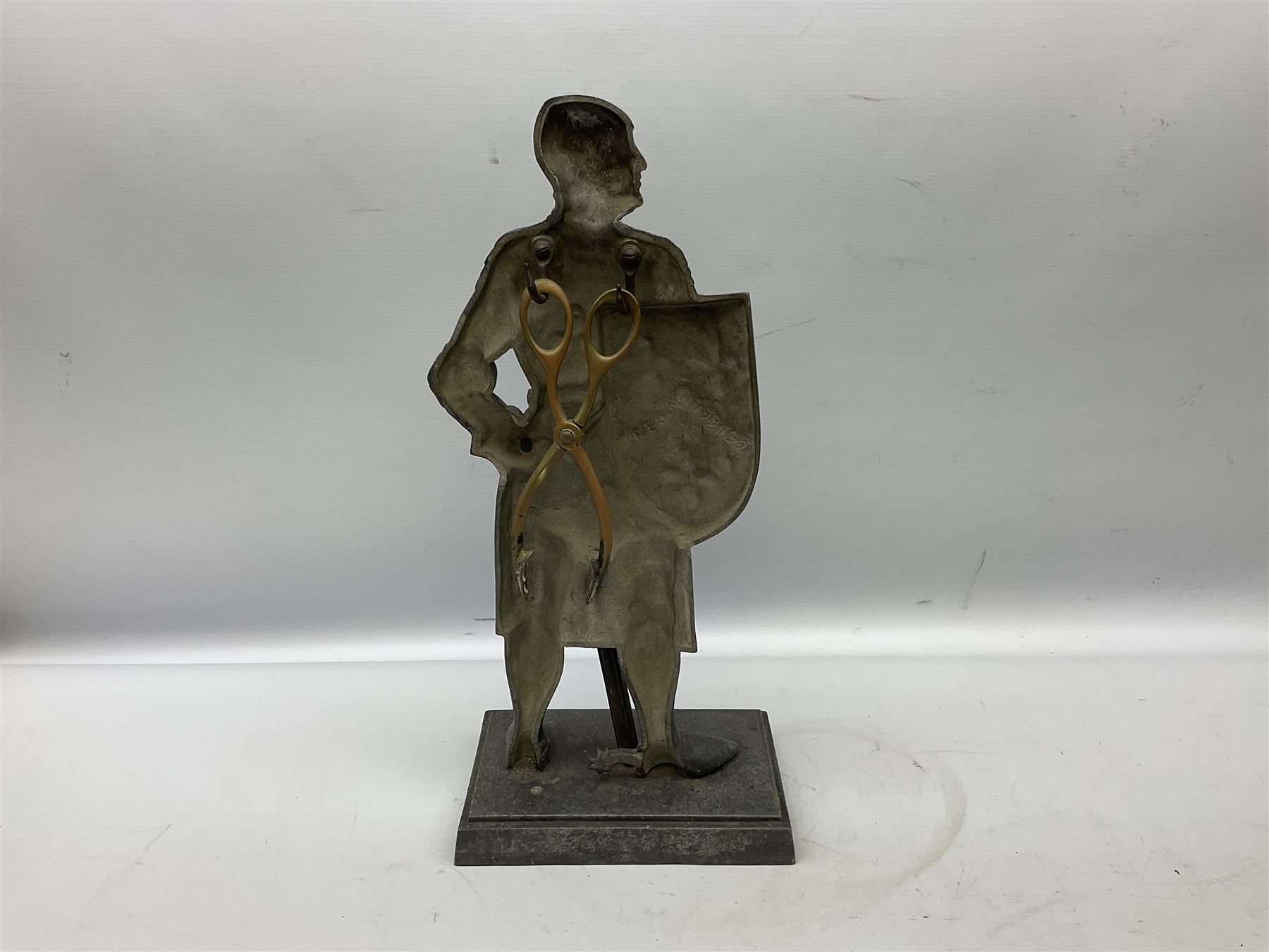 Cast iron fire companion set modelled as a knight in armour with fleur-de-lis shield and sword concealing fire poker, with brass tongs to reverse, raised upon stepped rectangular base, H55cm