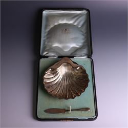 Edwardian silver butterdish in the form of a clam shell and upon four bun feet, hallmarked Williams Birmingham Ltd, Birmingham 1905, with a silver plated butter knife, contained within a fitted tooled leather case, width of dish 13cm