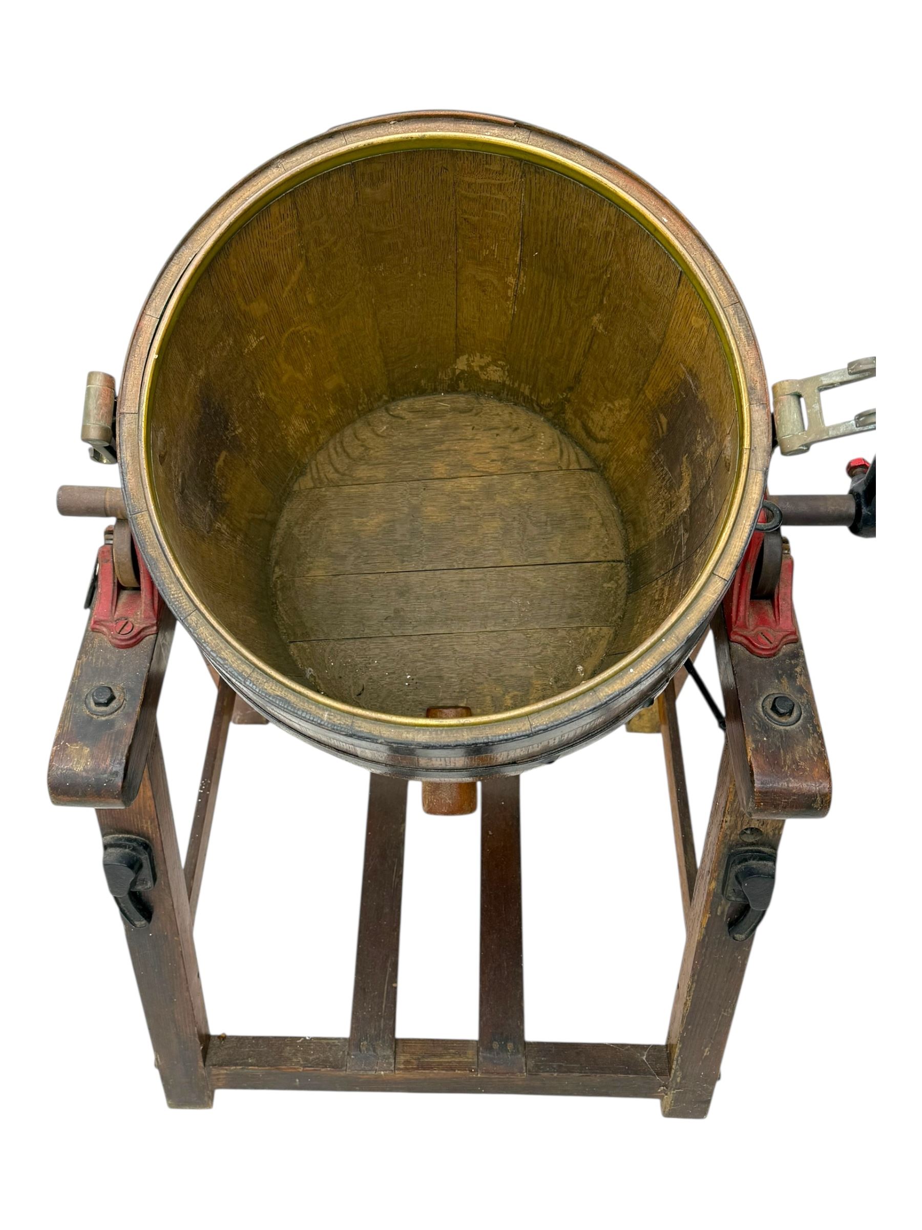 19th century oak and cast iron rotary butter churn, with coopered barrel body, domed lid with filler opening and cast iron securing arms, on tilting iron-mounted frame with crank handle and support rails
