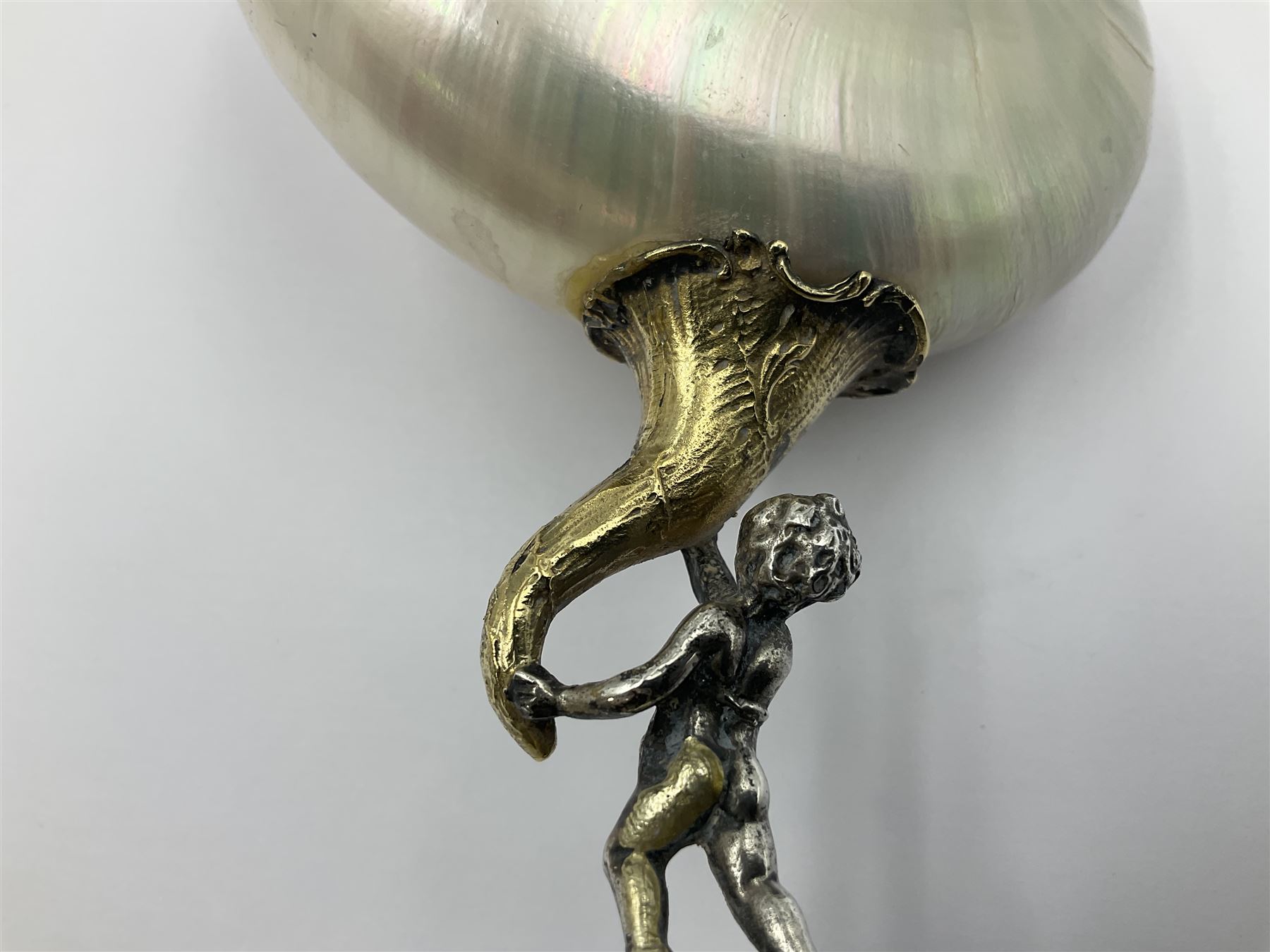Modern limited edition silver mounted nautilus shell cup, no. 42/150, the pearlescent shell cup with silver-gilt strapwork to rim, upon a stem modelled as a putto supporting a gilt cornucopia and circular domed foot depicting Poseidon amongst swirling waves, hallmarked by St James House Company, London 1980,  H17.5cm