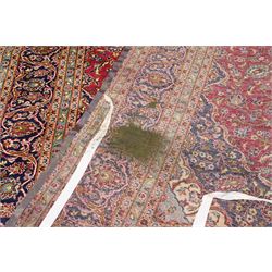 Persian Kashan hand-knotted carpet, madder red ground centred by shaped dark navy and ivory floral medallion with pendants, surrounded by scrolling vines, palmettes and flowerheads, dark navy spandrels, enclosed by dark navy floral border with multiple narrow floral guard stripes
