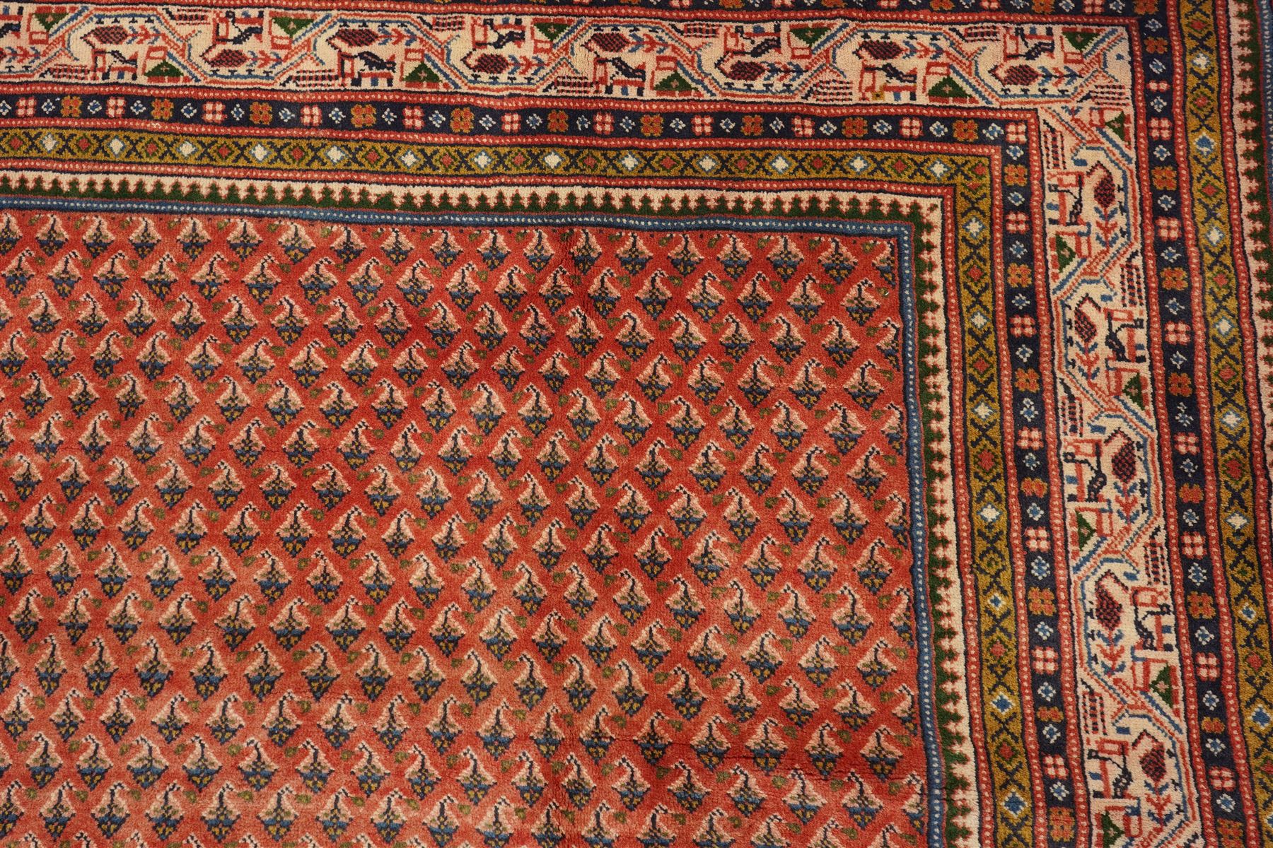West Persian Boteh-Mir hand-knotted rug, madder red field densely decorated with a repeating lattice of of small boteh motifs arranged in diagonal rows enclosed by a broad border of stylized geometric devices and angular floral ornament between multiple guard stripes with cotton fringe ends