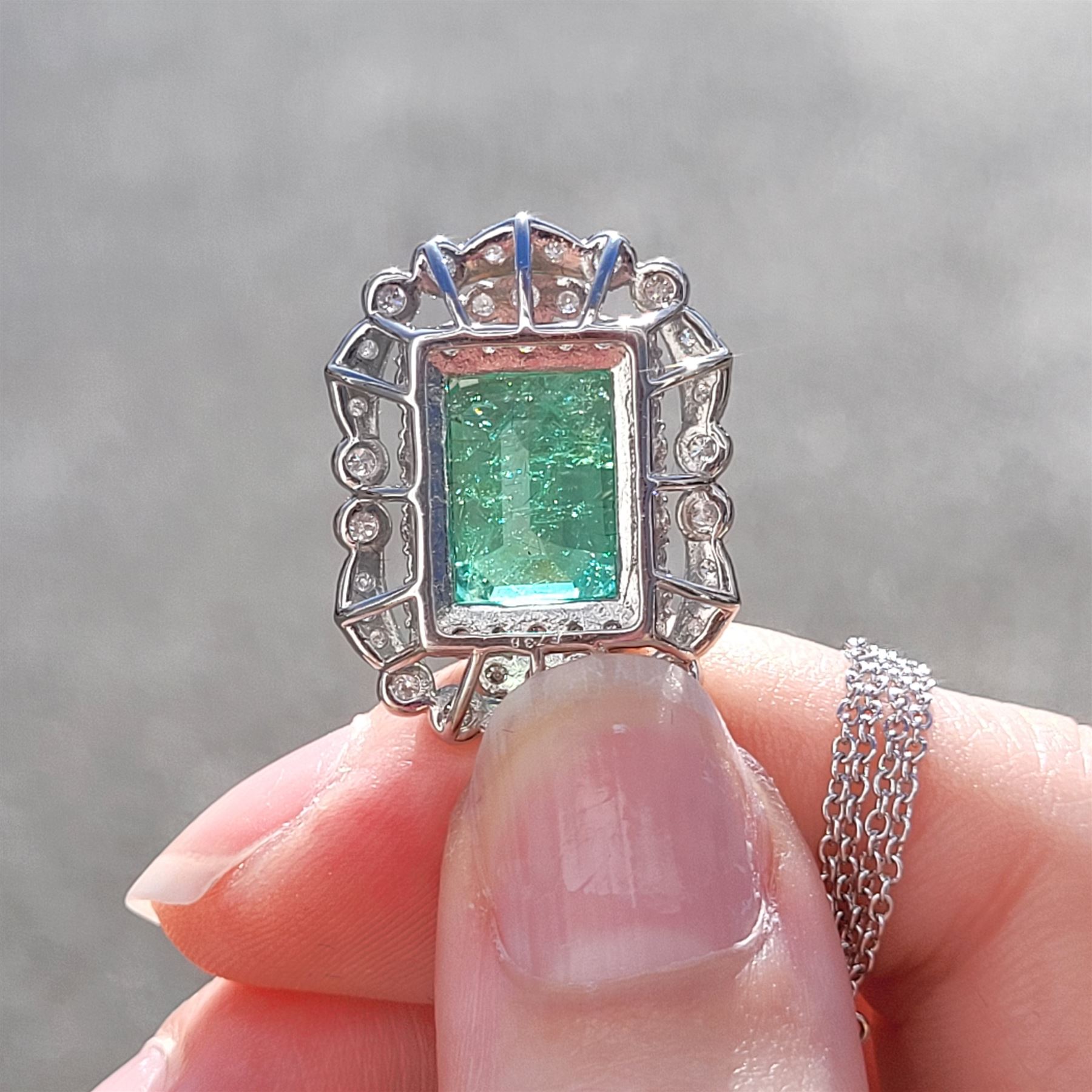 Platinum Colombian emerald and diamond pendant necklace, single octagonal cut emerald of 7.38 carat, surrounded by round cut diamonds in a fancy milgrain pierced design setting, stamped Pt 950, on a trace link chain necklace, total diamond weight 1.14 carat, with GCS certificate